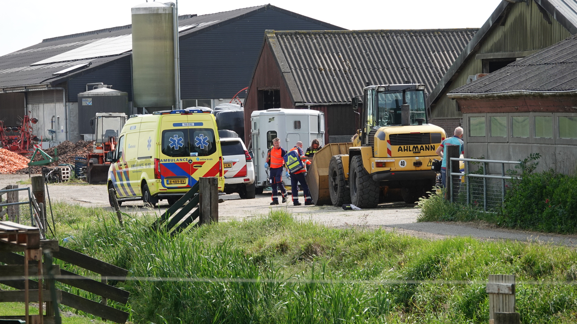 Ambulances en medische hulpverleners op een boerderij, met landbouwuitrusting en gebouwen op de achtergrond, tijdens een noodsituatie.