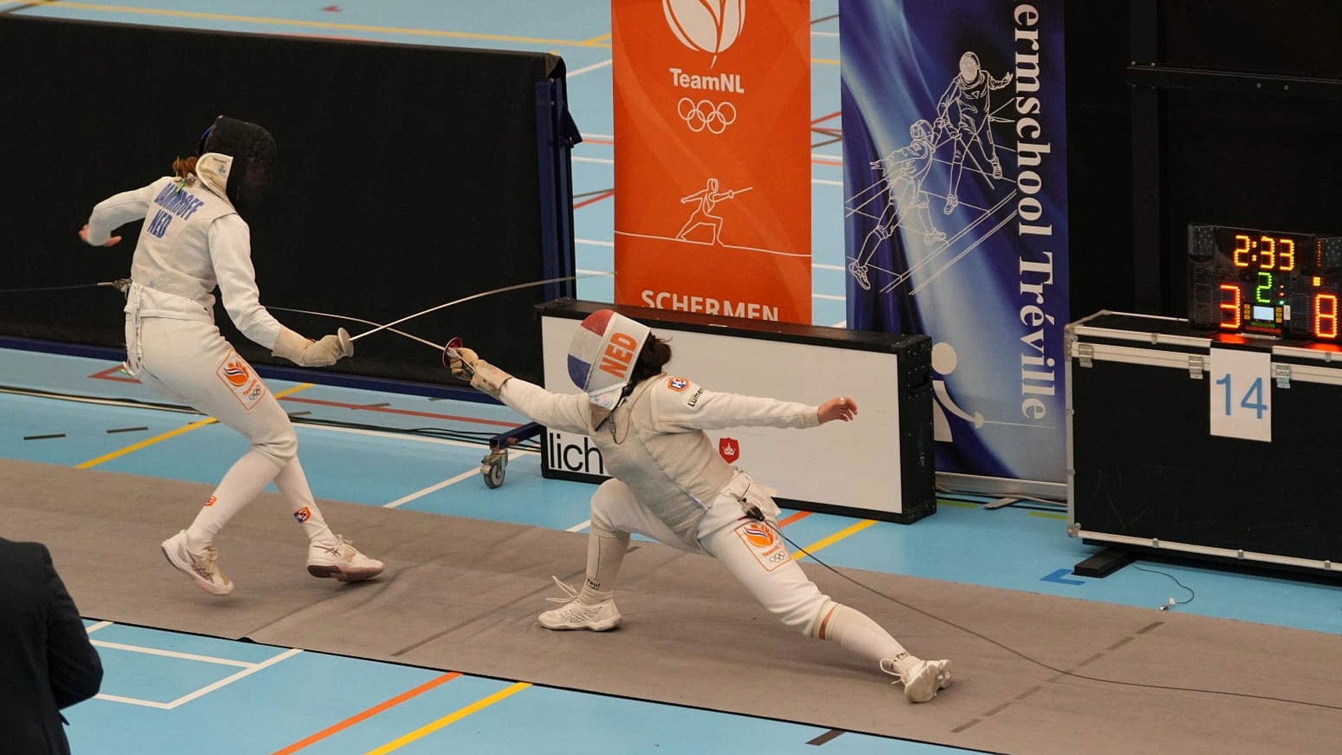 Twee schermsters in witte beschermende kleding tijdens een duel op een schermpiste, met een digitale scorebord en TeamNL spandoeken op de achtergrond.