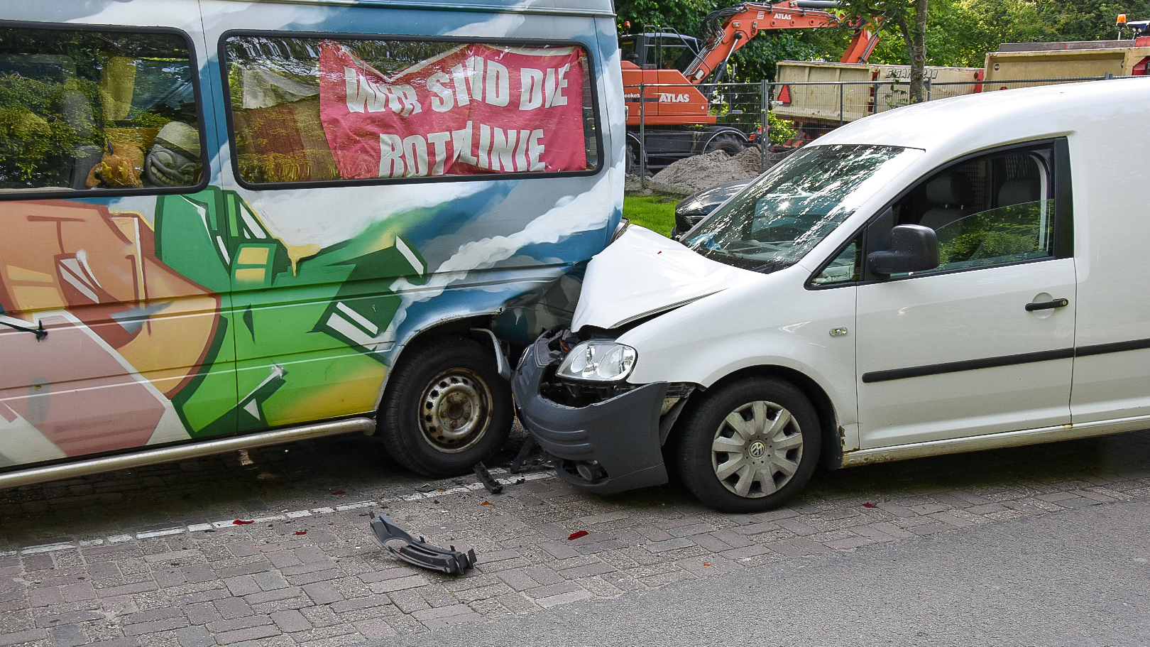 Een witte bestelwagen botst tegen een kleurrijk beschilderde bestelbus met een spandoek erin, op een straat met een beschadigde bumper vooraanzicht.