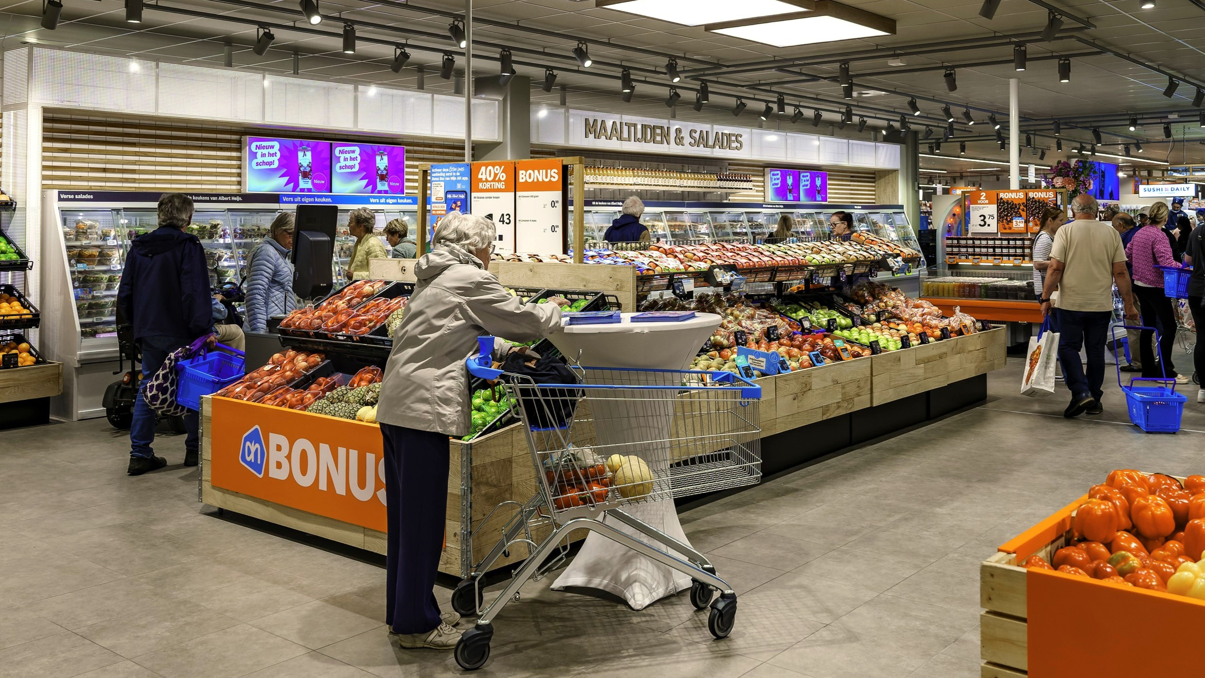 Mensen winkelen in een supermarkt met versafdelingen vol groenten en fruit.