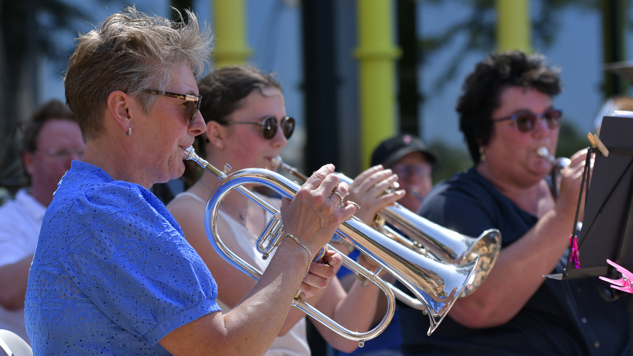Mensen spelen koperblazers in een orkest, met een vrouw in blauw als prominente figuur.