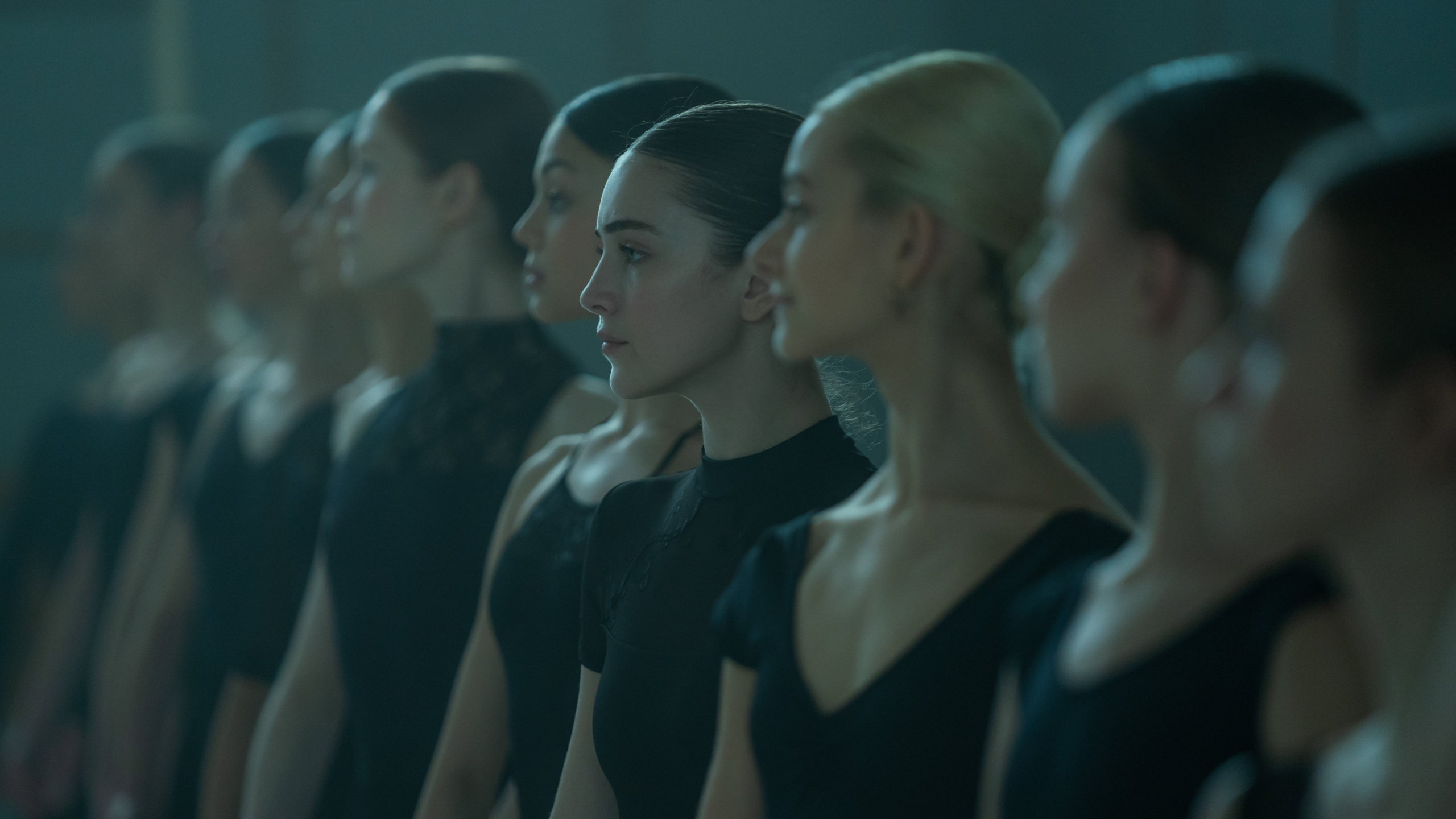 Een rij jonge dansers in zwarte kleding kijkt geconcentreerd naar voren in een dansstudio.