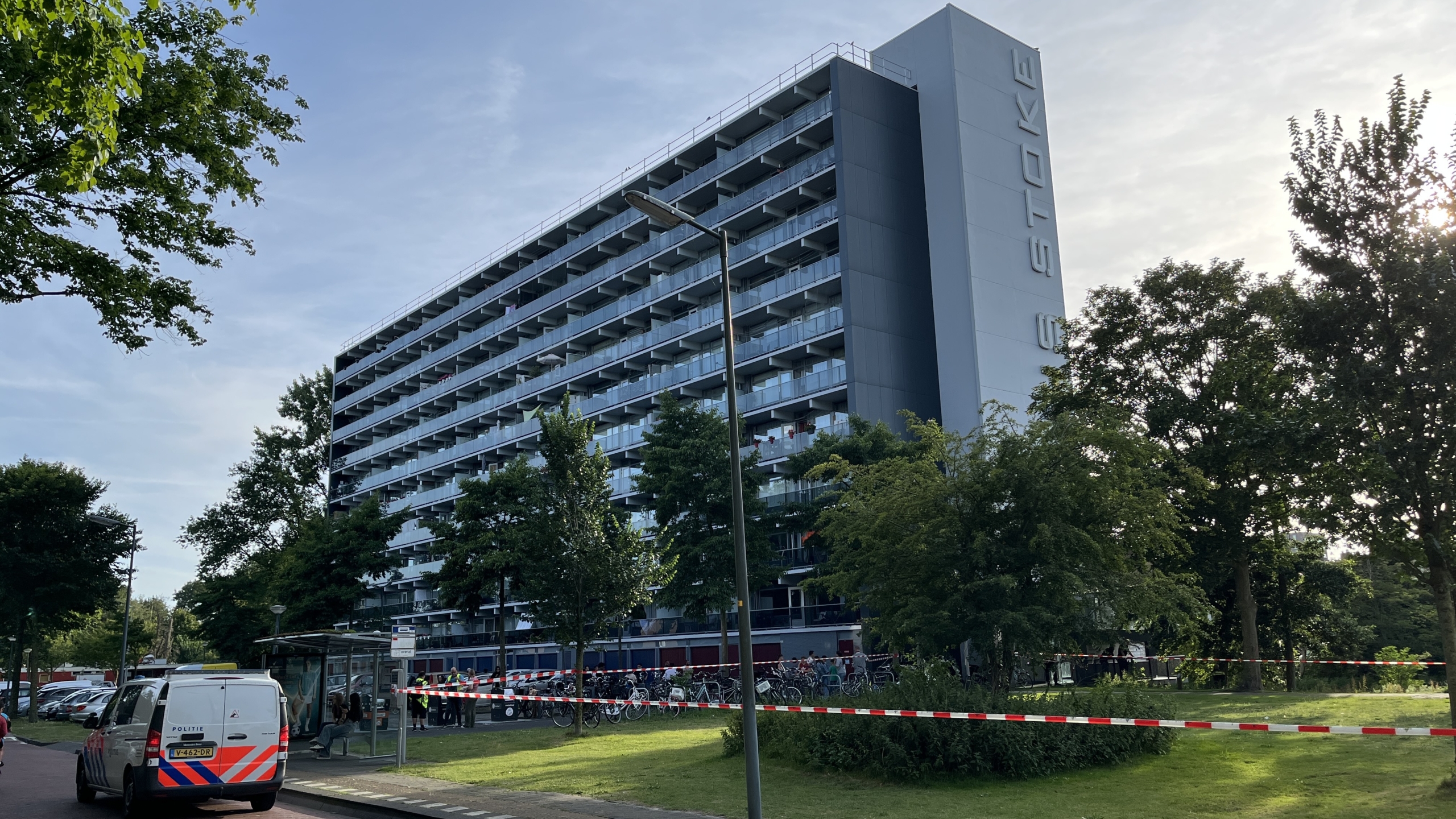Een groot flatgebouw omgeven door bomen met een politieauto geparkeerd op de weg ernaast. Het gebied is afgezet met rood-wit politielint.