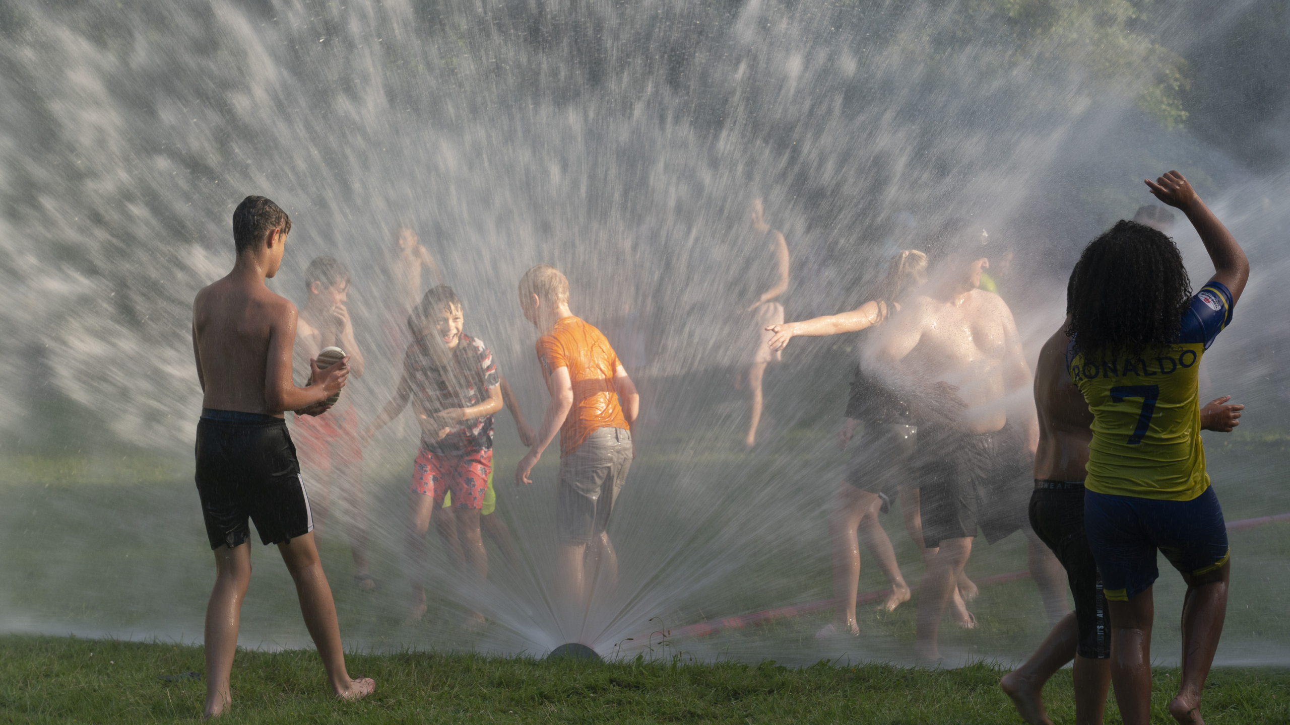 Kinderen spelen in het water van een grote sproeier in een zomerse omgeving.