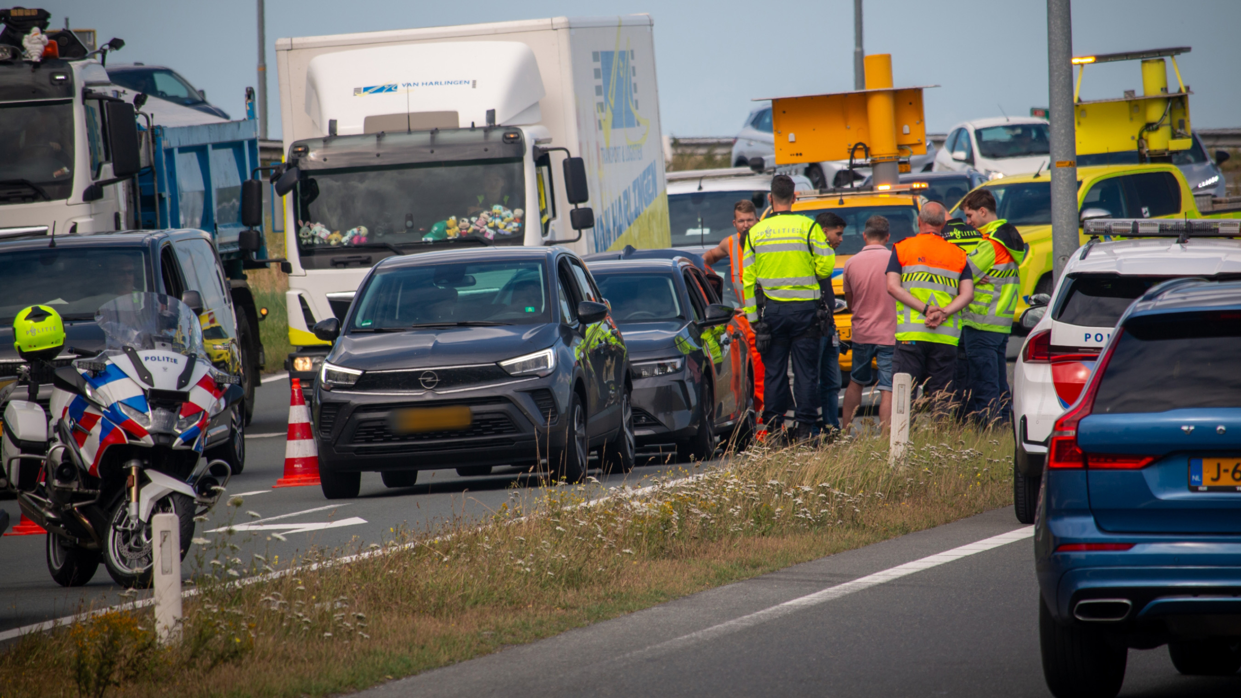 Voertuigen en politie op een snelweg bij een verkeersincident, met mensen in veiligheidshesjes die de situatie bespreken.