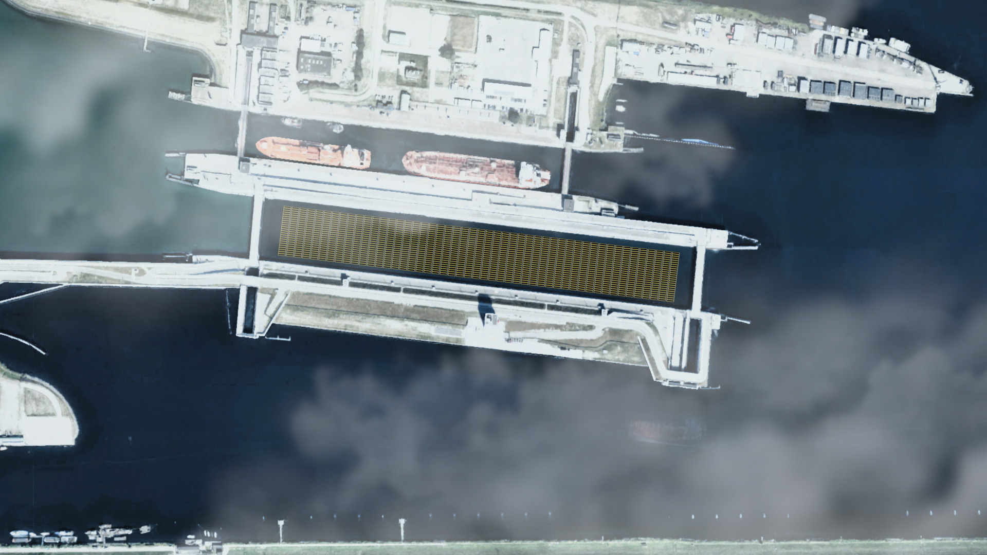 Luchtfoto van een kanaal met twee grote schepen aangemeerd, omgeven door gebouwen en wegen, met zichtbare wolken boven het water.