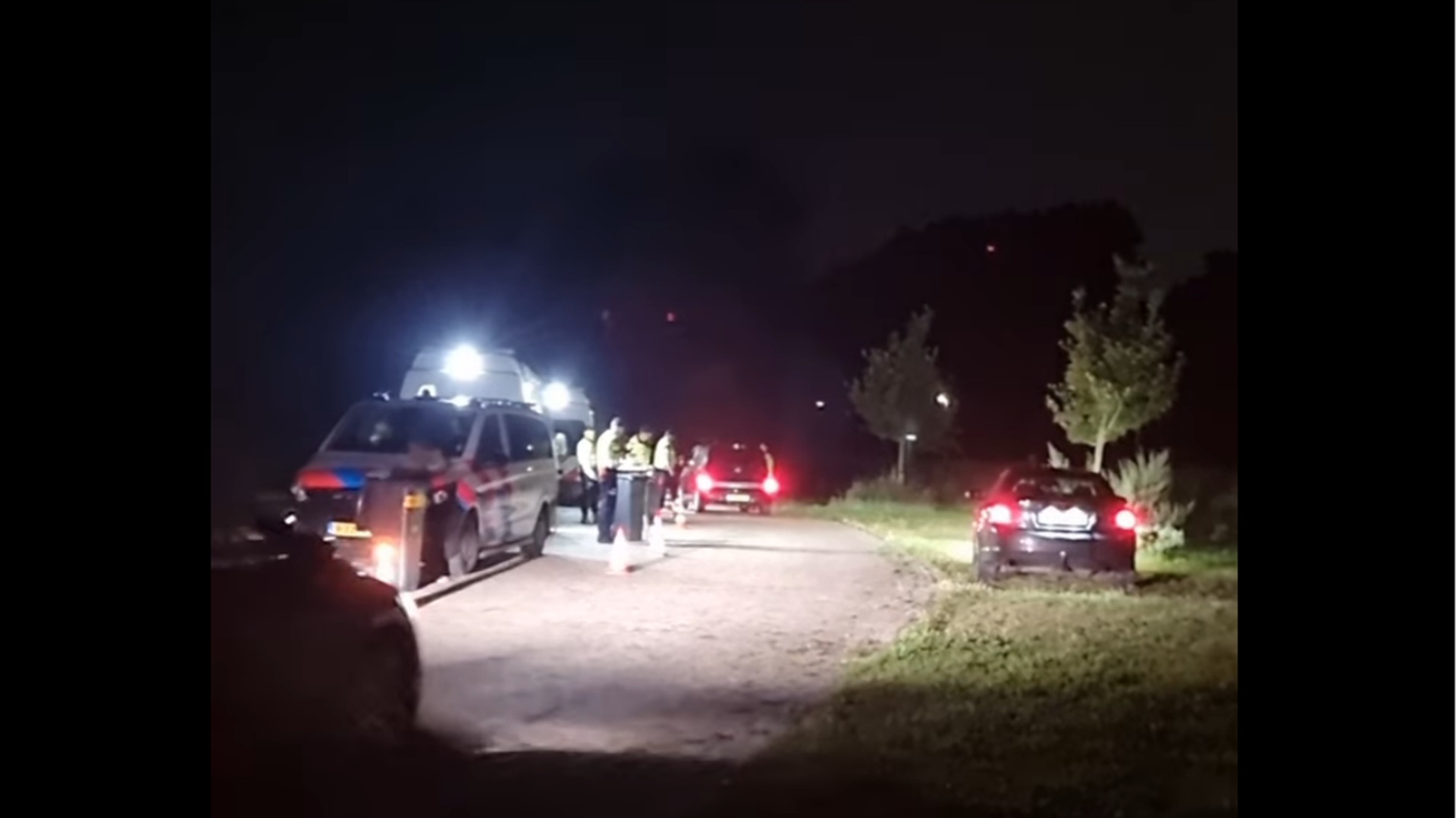 Een nachtelijke verkeerscontrole met politievoertuigen en agenten op een onverlichte weg.