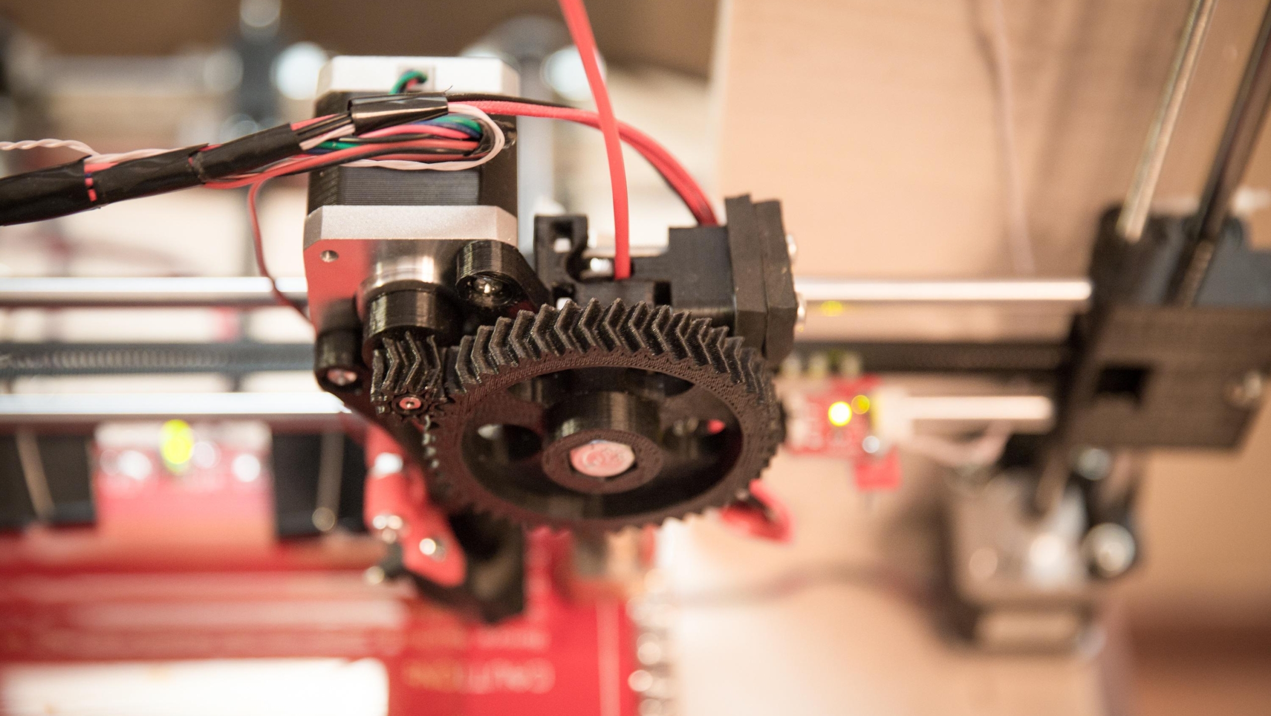 Close-up van een 3D-printerkop met zichtbare bedradings en tandwielen.