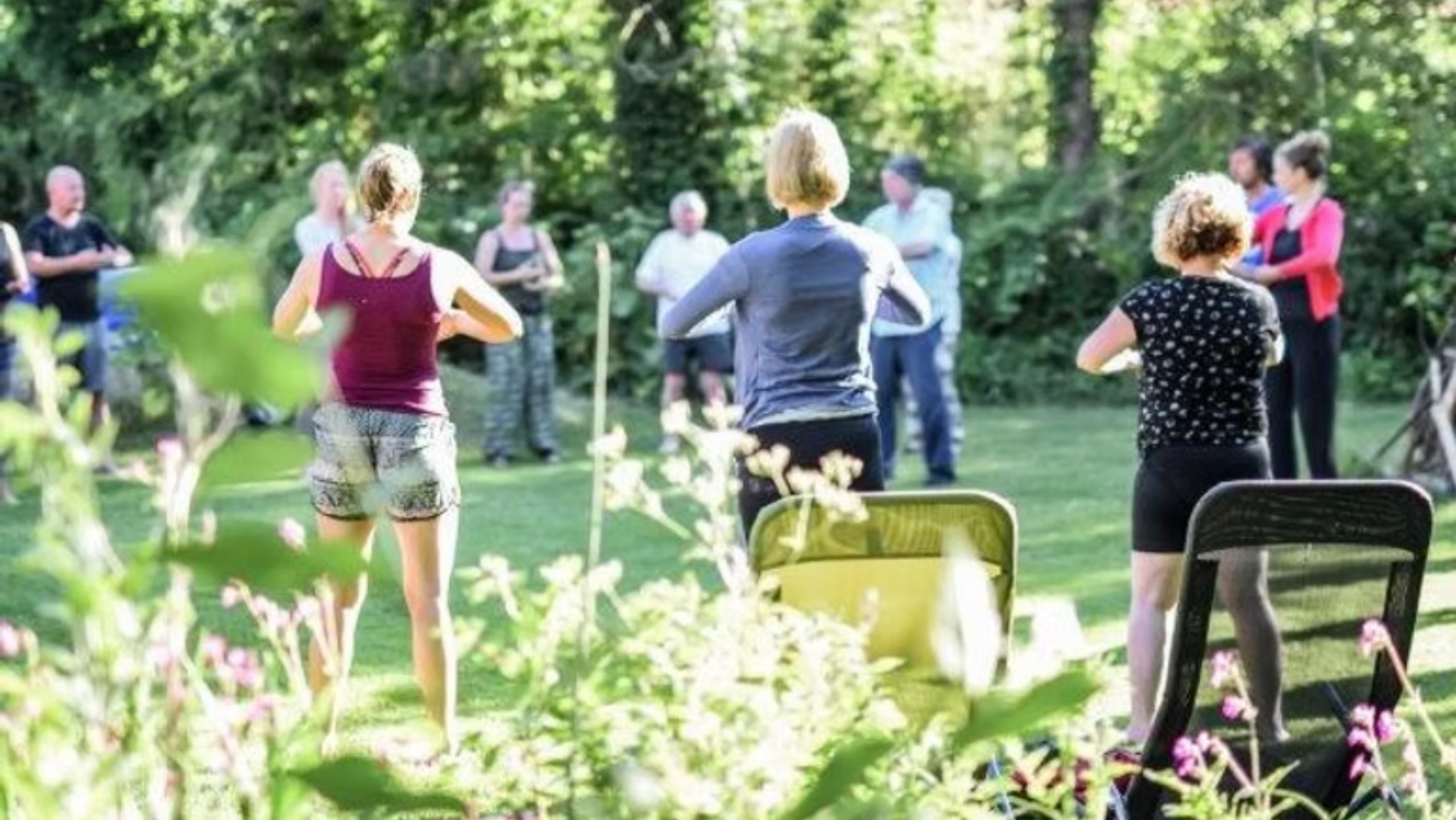 Mensen in een tuin doen samen tai-chi onder de bomen en zonlicht.