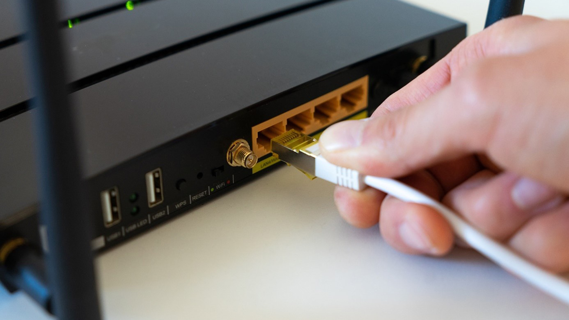 Hand steekt een ethernetkabel in een poort van een wifi-router.