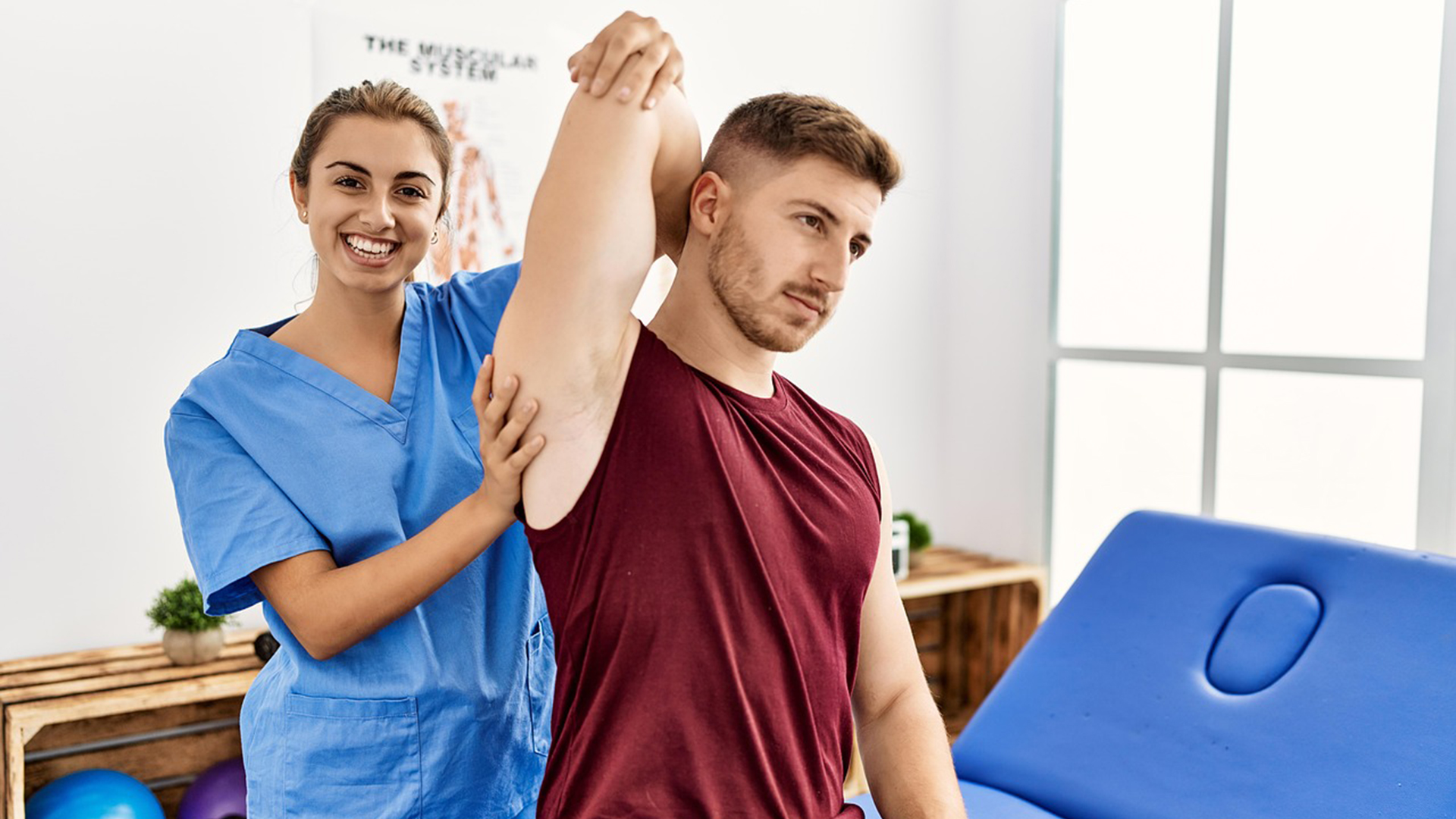 Een fysiotherapeut helpt een mannelijke patiënt met een armstretch in een lichte behandelkamer.