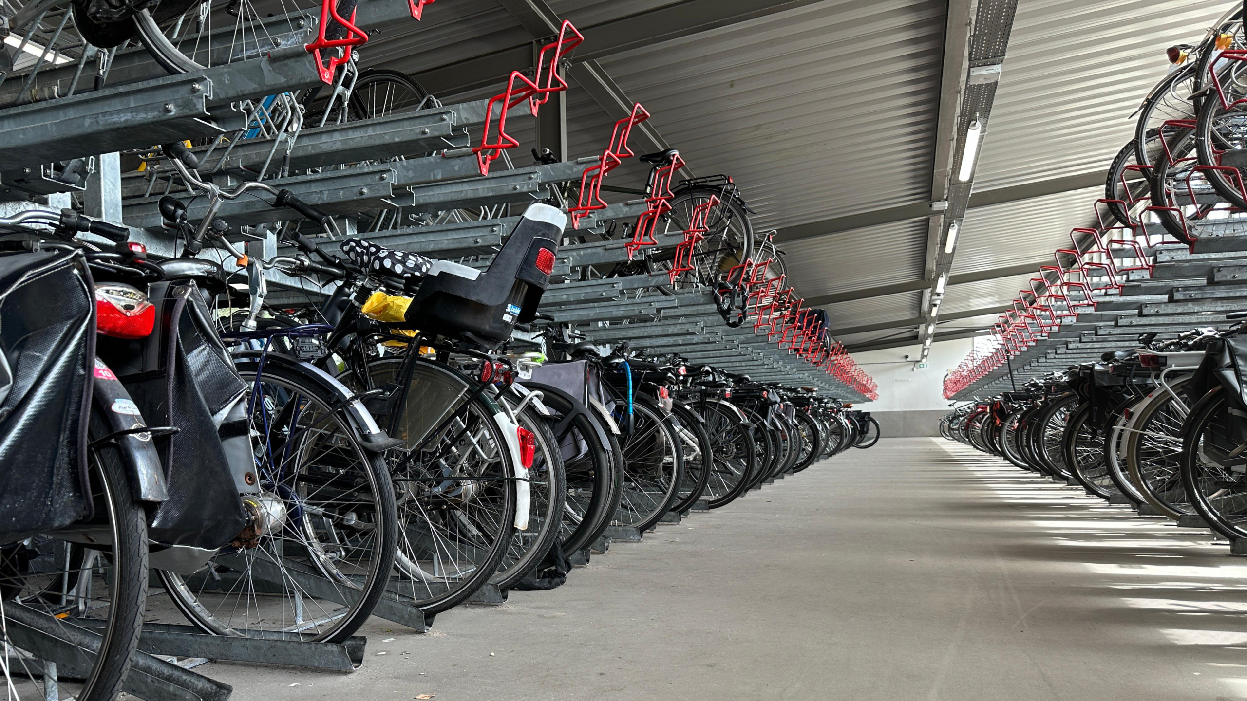 Een overdekte fietsenstalling met rijen fietsenrekken, waarin meerdere fietsen zijn geparkeerd, zowel op de grond als op bovenste verdiepingen van het rek.