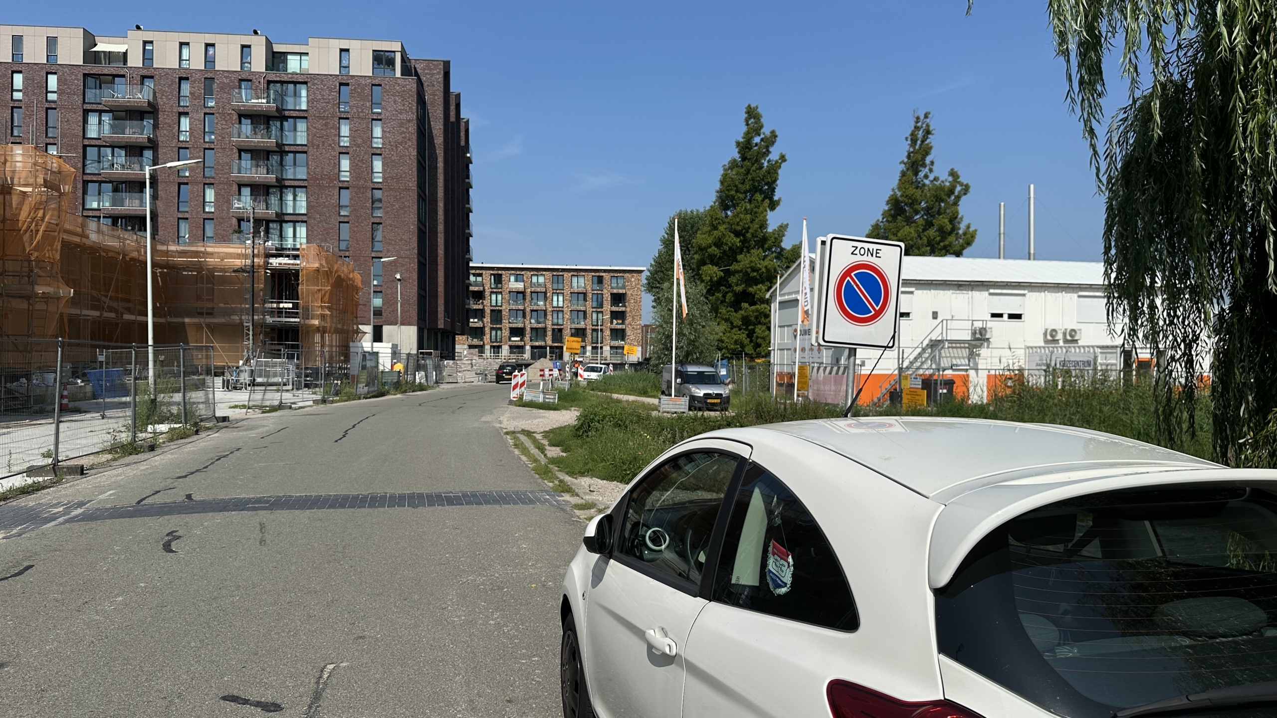 Wooncomplex in aanbouw naast een weg met een geparkeerde witte auto en een zonebord op de voorgrond.