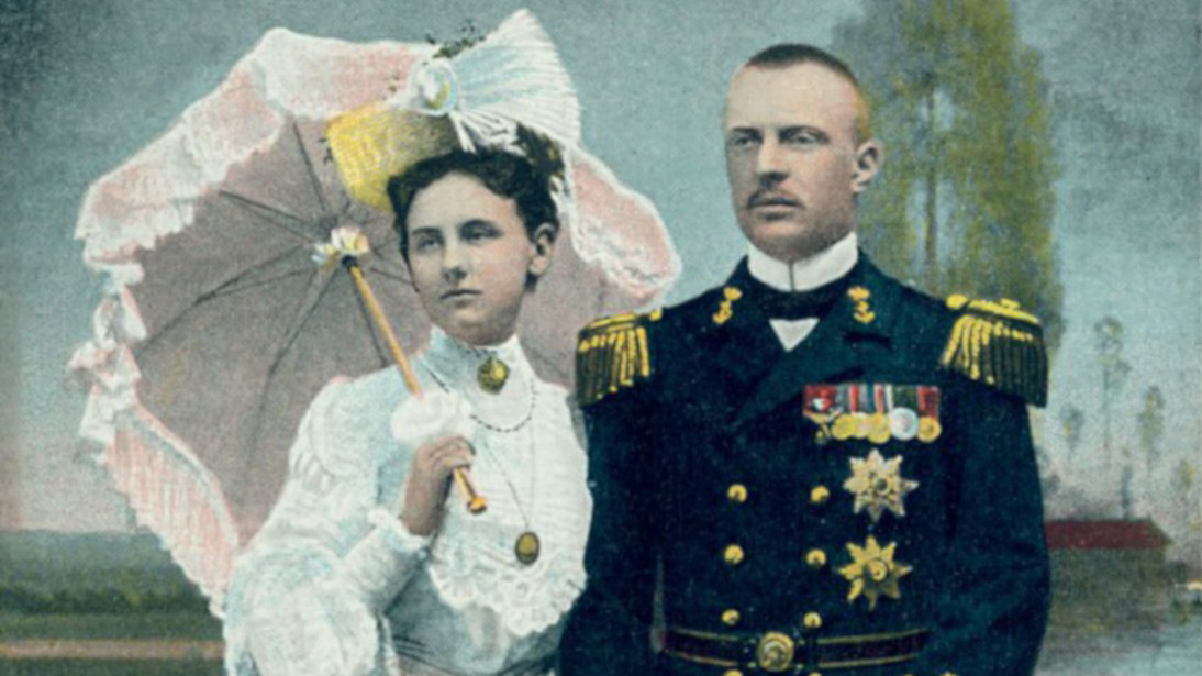 Een man in een marine-uniform staat naast een vrouw in een elegante witte jurk, die een parasol vasthoudt. Beiden kijken in de verte. Op de achtergrond is een tuinscène te zien.