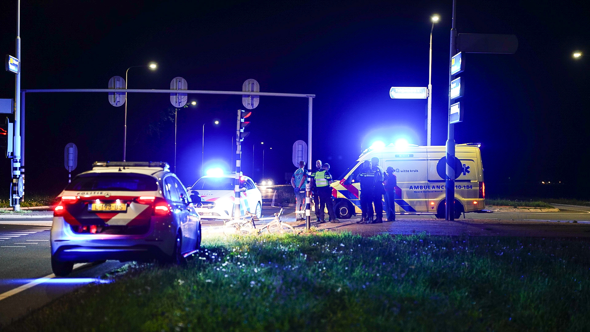 Politie en ambulance bij een verkeersongeluk in de nacht, met voertuigen die felblauwe zwaailichten uitstralen.