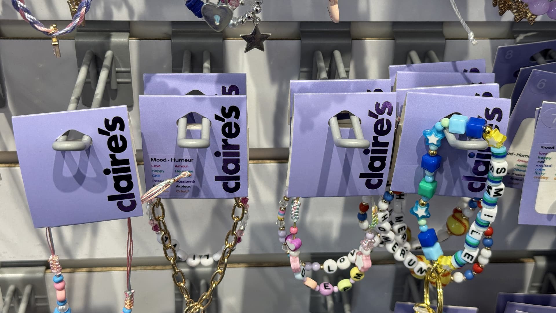 Een display van kleurrijke armbanden en kettingen met kralen, gepresenteerd op lavendelkleurige kaartjes gemarkeerd met "Claire's" in een winkel.