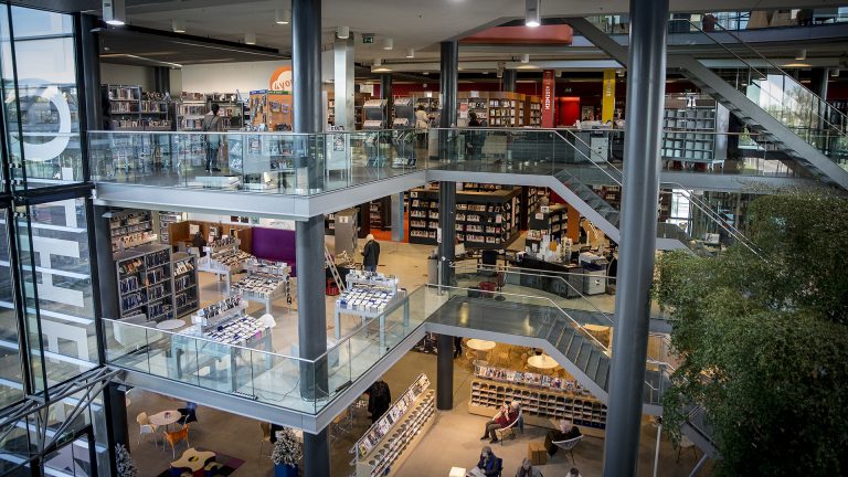 Een moderne bibliotheek met meerdere verdiepingen, glazen balustrades en een ruime, open structuur vol boekenplanken en leesstoelen.
