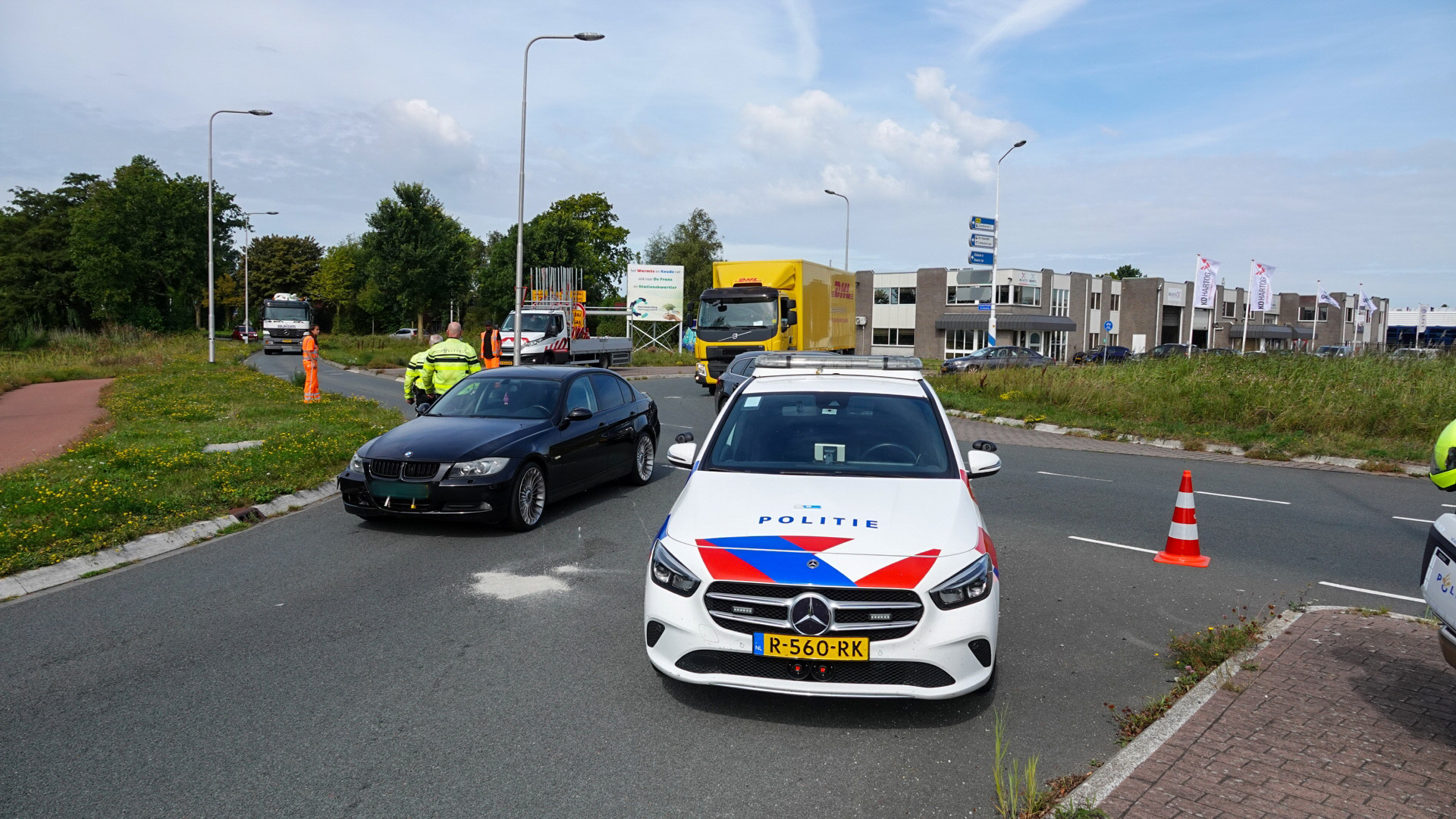 Politieauto en andere voertuigen op een weg, met enkele verkeerskegels en personen in fluorescerende kleding bij een verkeerscontrole.
