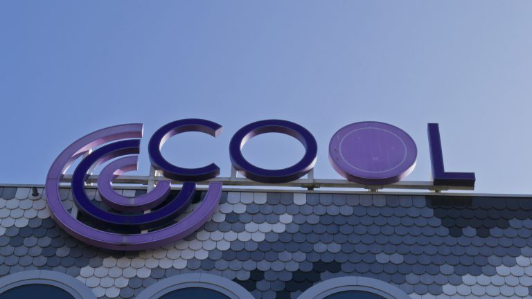 Bord met het woord 'COOL' in paarse letters op een gebouw met een blauwe lucht op de achtergrond.