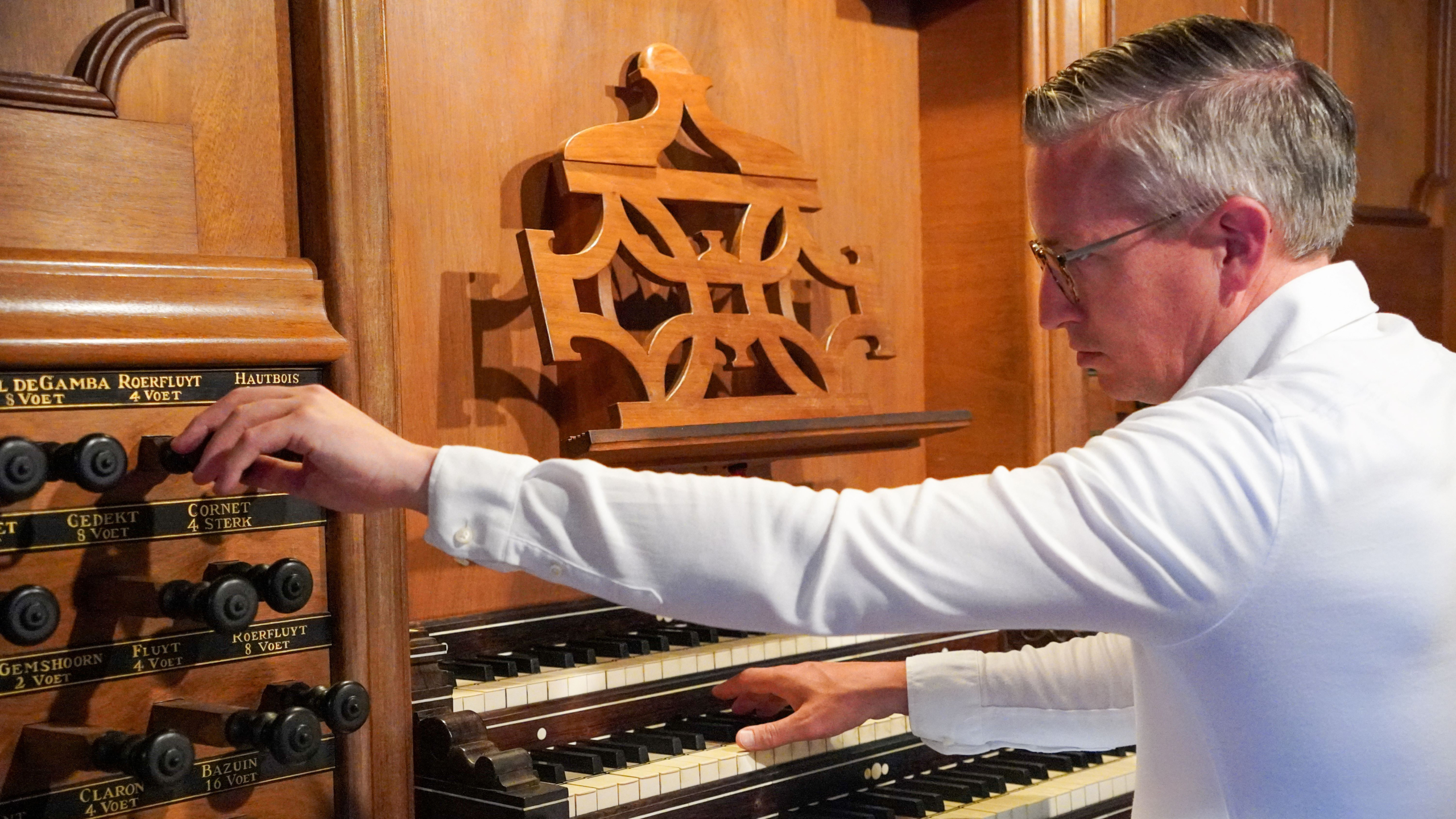 Een man speelt een kerkorgel, waarbij hij registers bedient en de toetsen bespeelt, terwijl hij zich concentreert op het instrument.