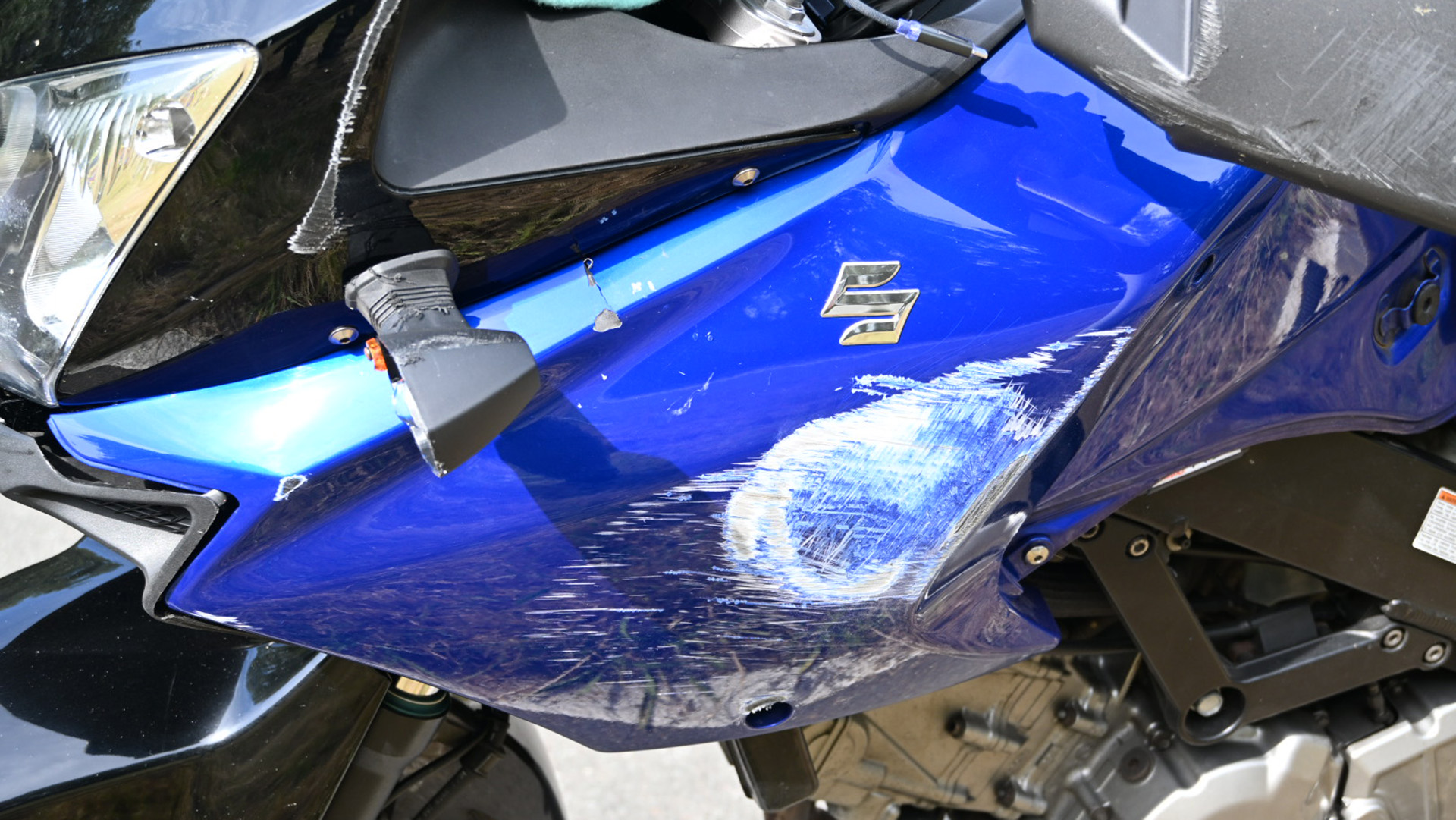 Blauwe motor met zichtbaar schade aan de zijkant, inclusief krassen en lakschade, met een merklogo op de beplating.