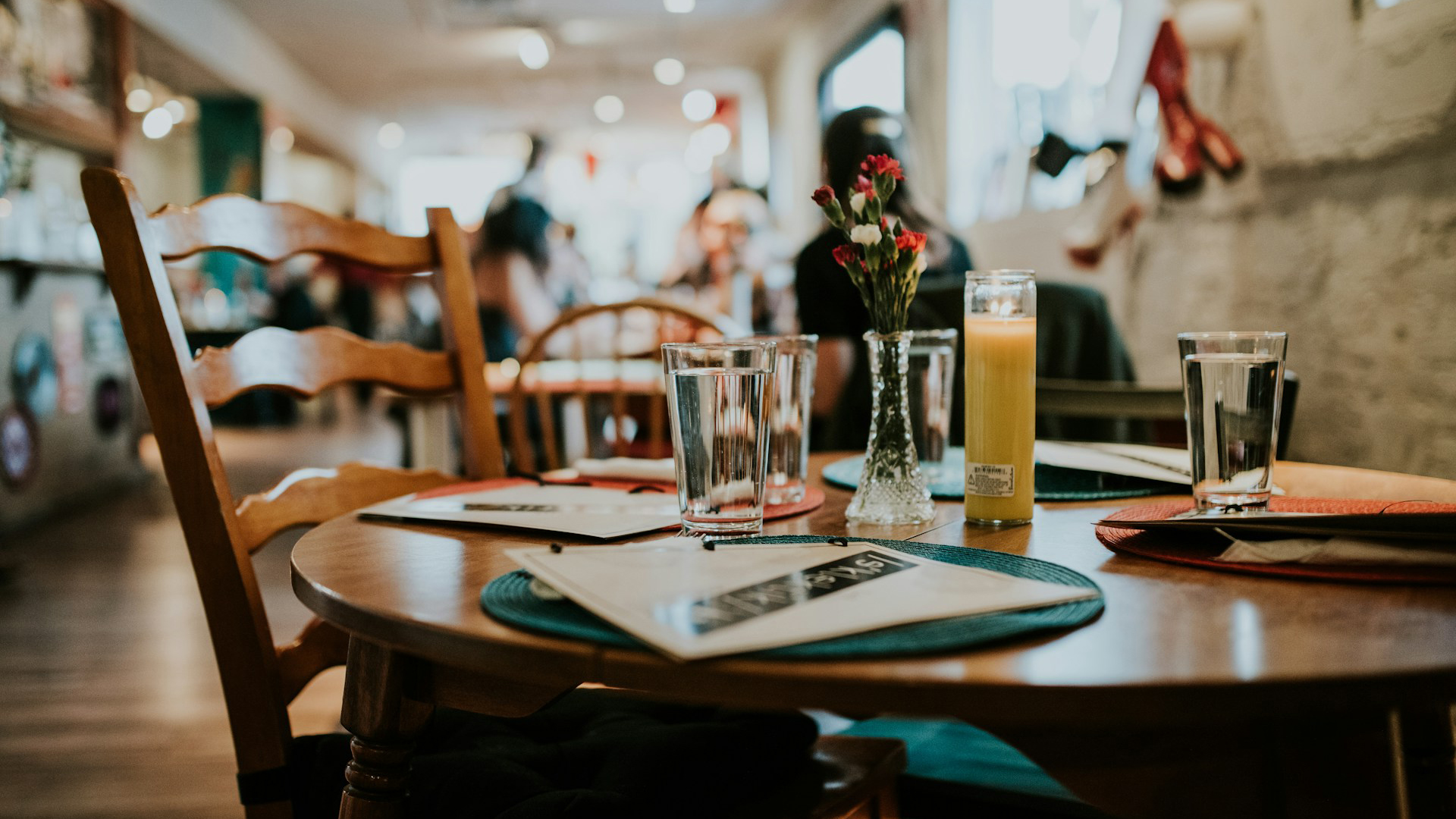 Een gezellig gedekte tafel in een café met glazen water, een brandende kaars, een vaas met bloemen en menukaarten.
