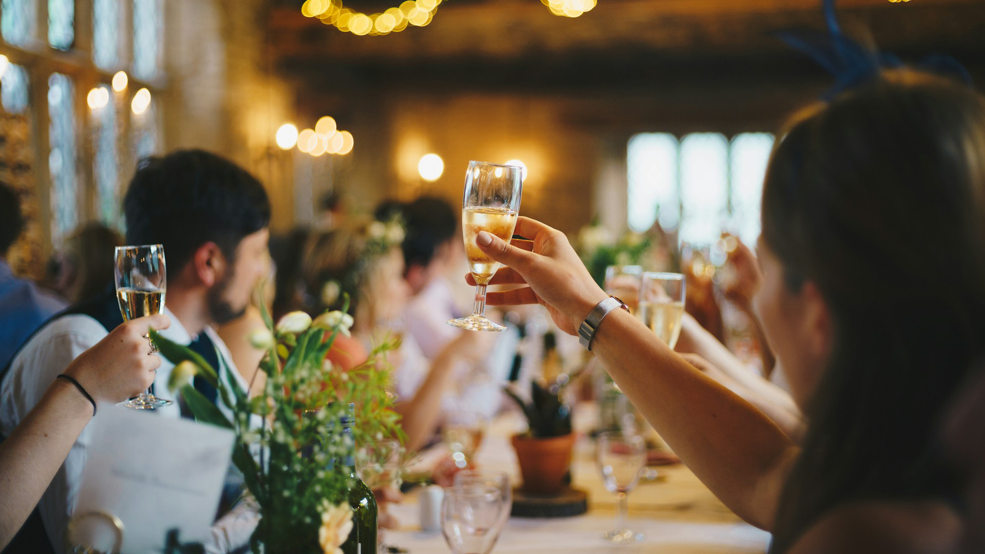 Groep mensen tilt glazen champagne op tijdens een feestelijke toast in een sfeervol ingerichte zaal.