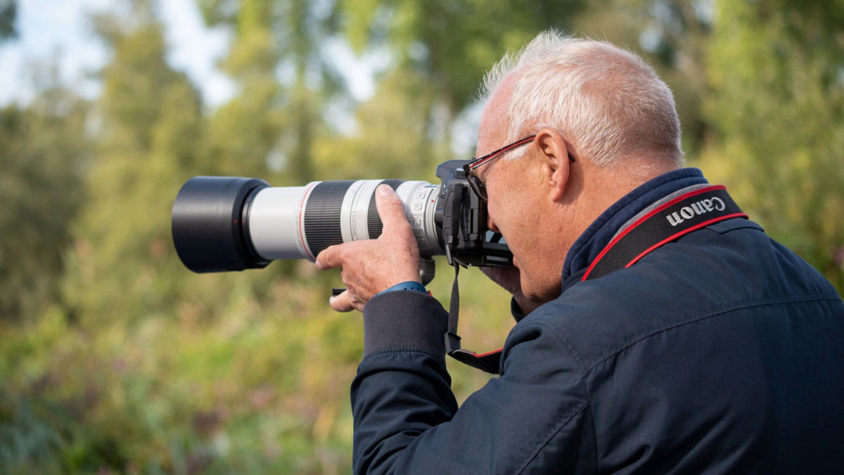 Man maakt een foto met een Canon-camera met een grote telelens in een groene buitenomgeving.