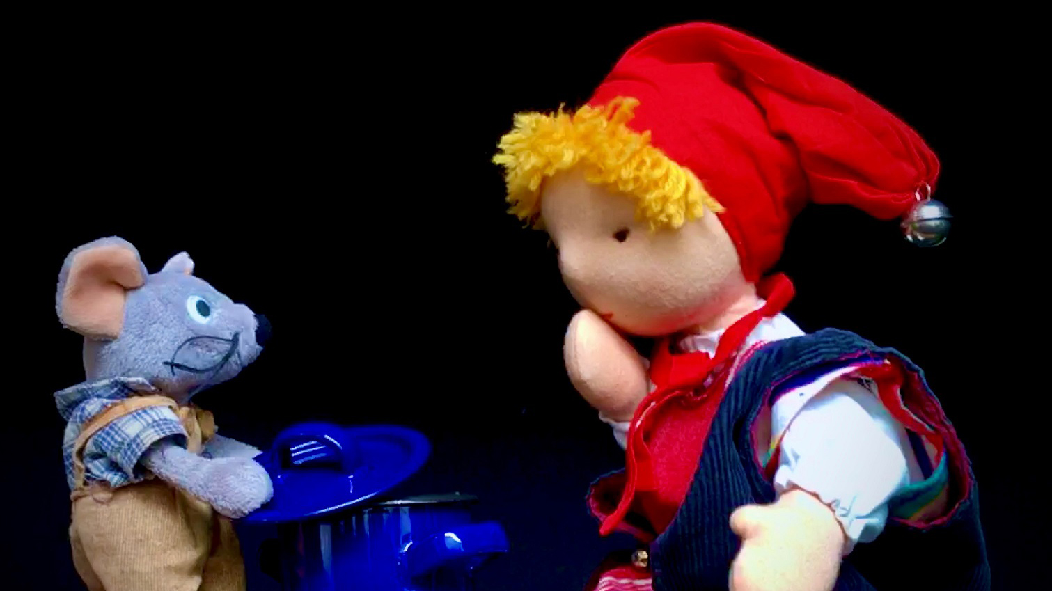 Poppenspel met een knuffelmuizenkus en een roodgeklede pop met een muts, zittend voor een blauwe pot.