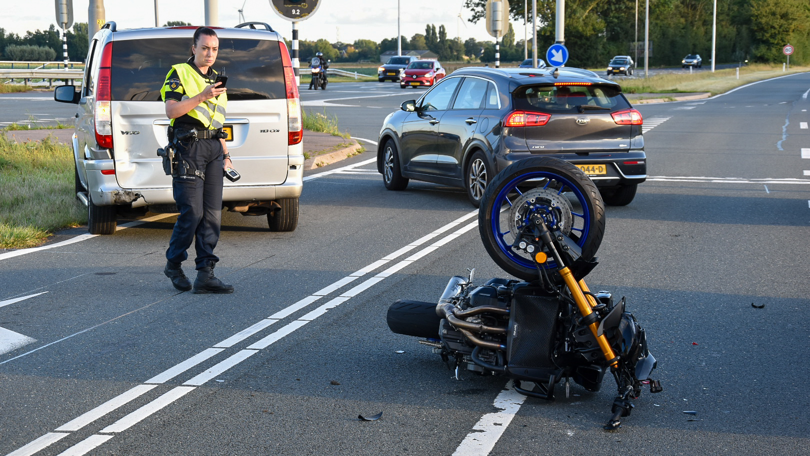 Een politieagent staat bij een omgevallen motorfiets op een kruispunt, met auto's op de achtergrond.