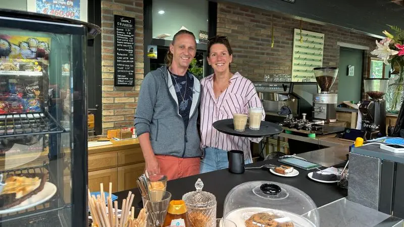 Twee mensen staan glimlachend achter de toonbank van een café, met koffie en gebak zichtbaar op de voorgrond.