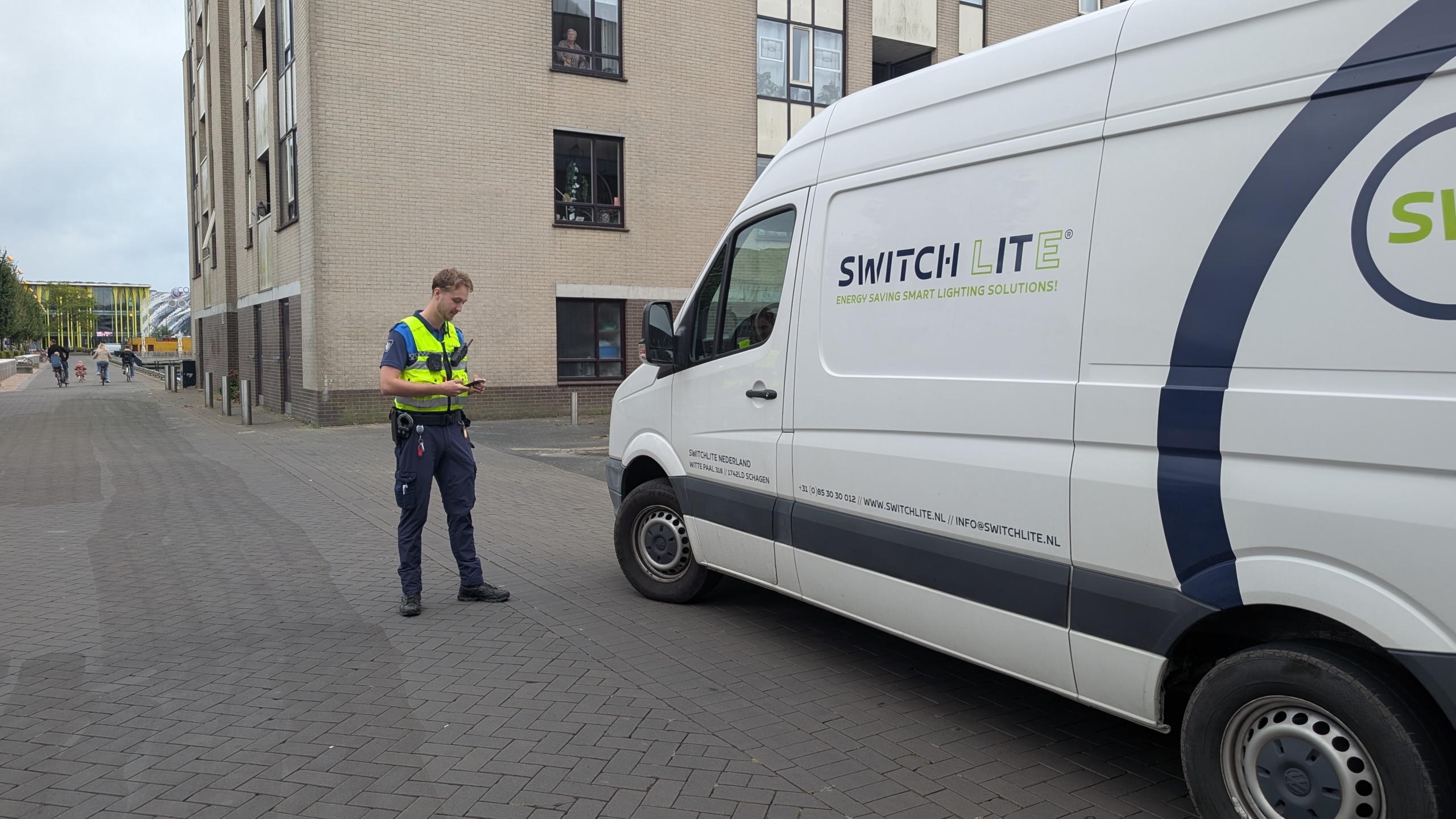 Een handhaver staat naast een geparkeerde bestelwagen van Switch Lite in een straat, met een woongebouw op de achtergrond.