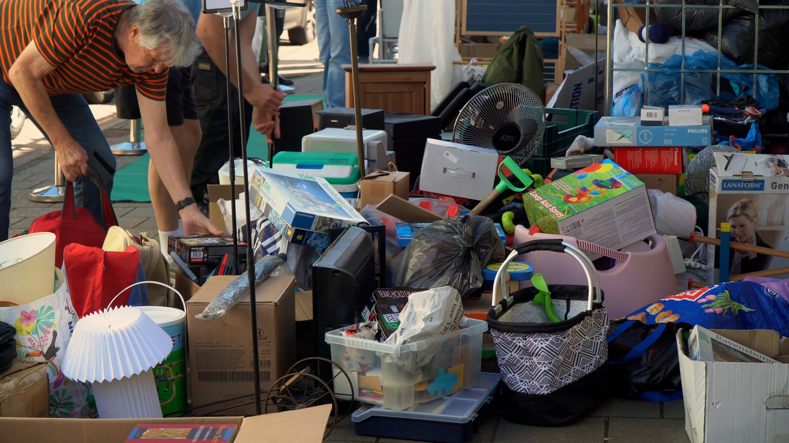 Een man zoekt tussen stapels tweedehands spullen en dozen op de rommelmarkt.