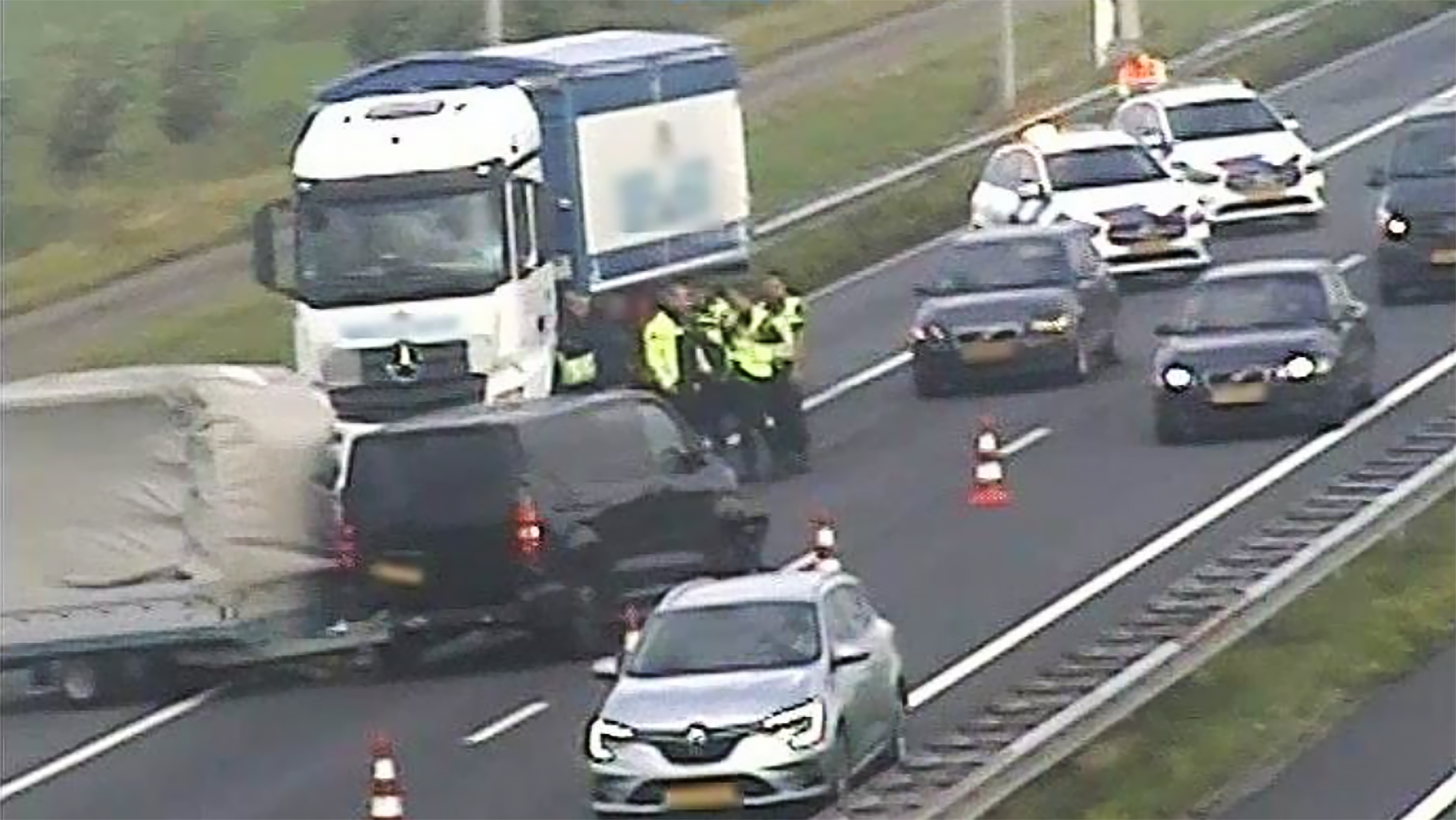 Autos en een vrachtwagen staan stil op een snelweg, omringd door politieagenten in reflecterende jassen, met verkeerskegels op de weg.