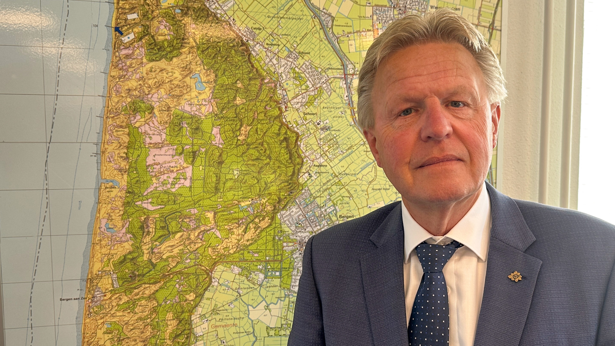Een man in een blauw pak staat voor een gedetailleerde kaart aan de muur.