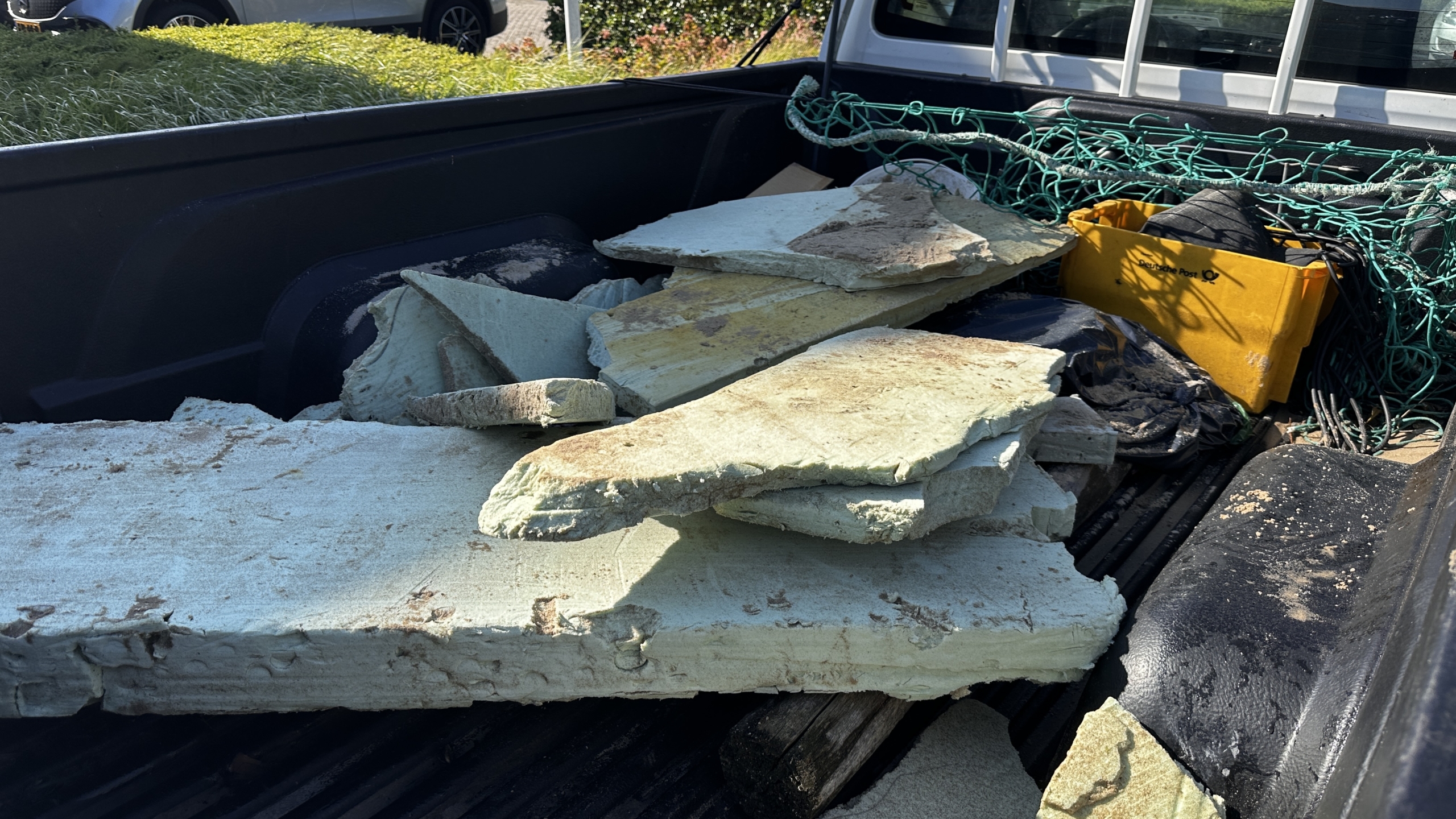 Schuimblokken en andere materialen liggen in de laadbak van een voertuig, samen met een geel krat en groene netten.