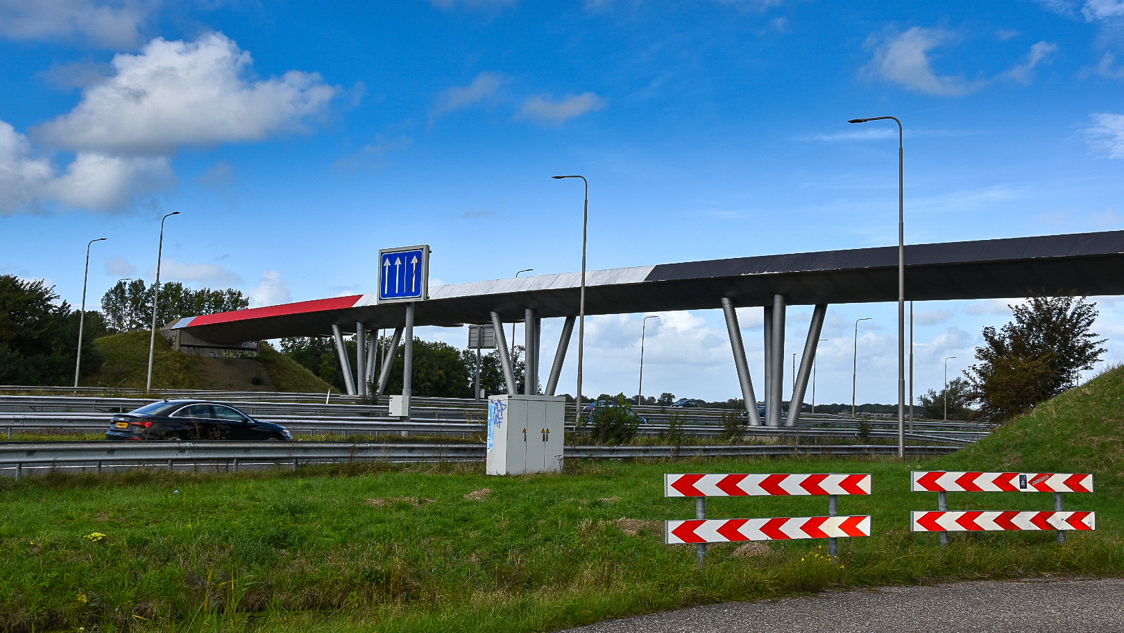 Een snelweg met een viaduct erboven, voorzien van opvallende rode en witte decoratie, onder een blauwe lucht met enkele wolken.