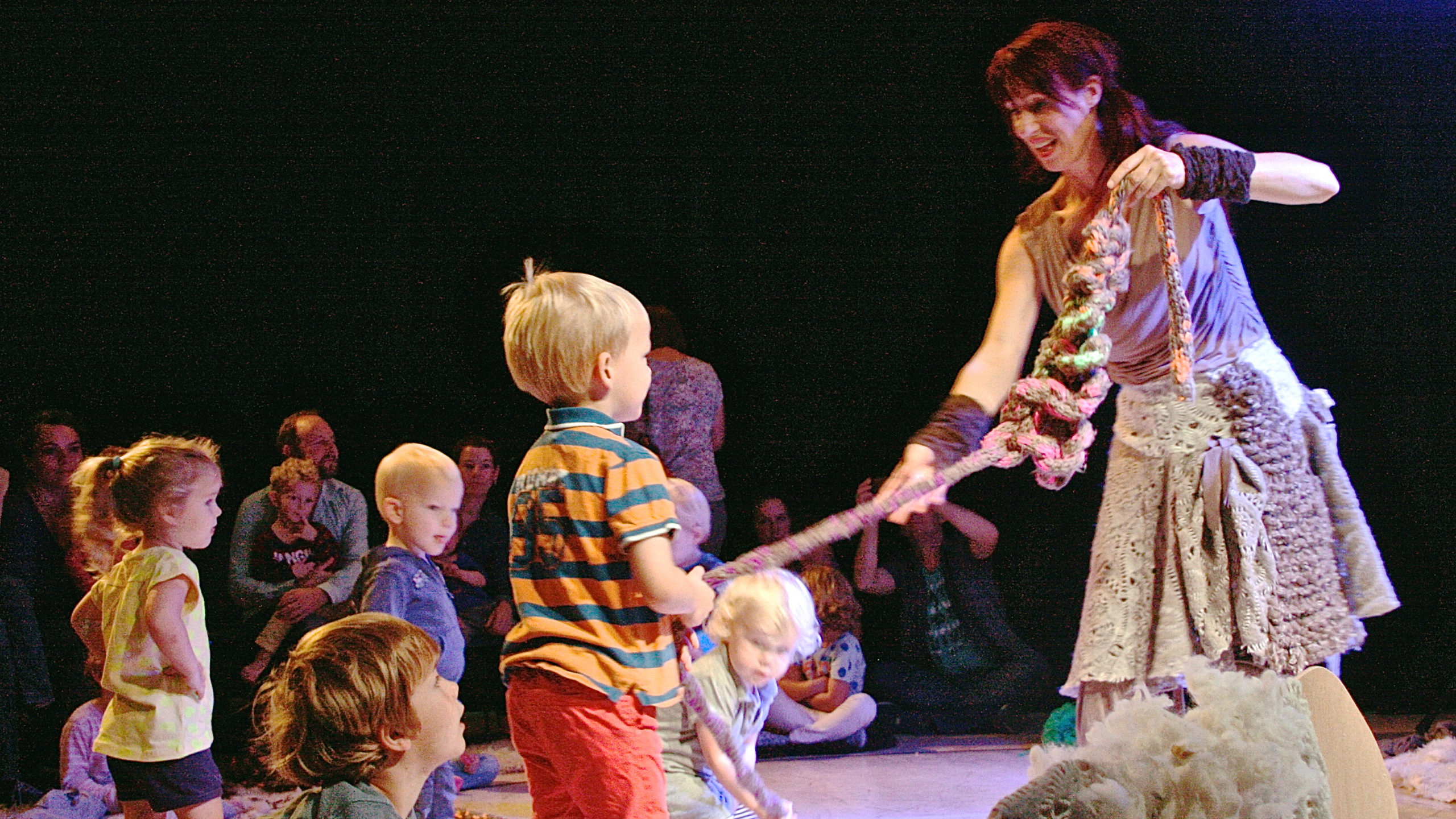 Een performer met gevlochten touw entertaint een groep kinderen op een podium, waarbij de kinderen actief meedoen.