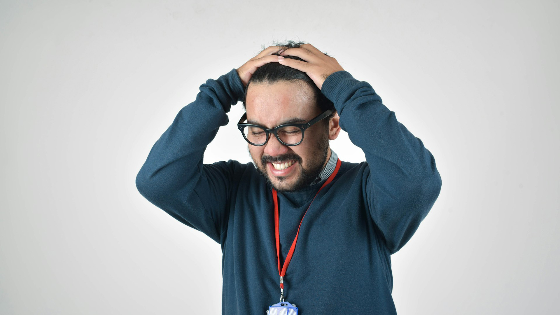 Man met bril en blauwe trui houdt zijn handen op zijn hoofd met een bezorgde uitdrukking.