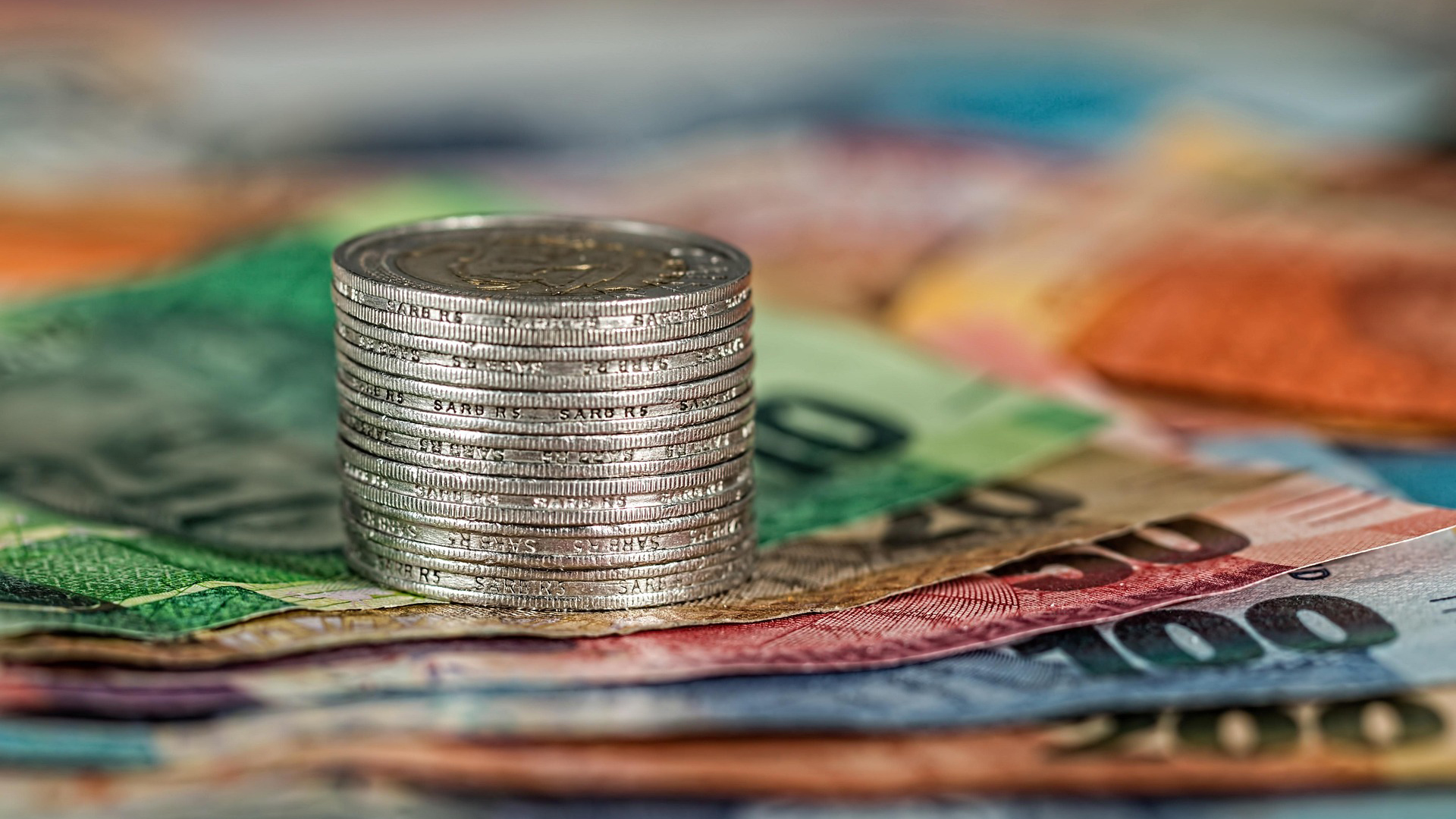 Een stapel zilveren munten ligt op kleurrijke bankbiljetten.