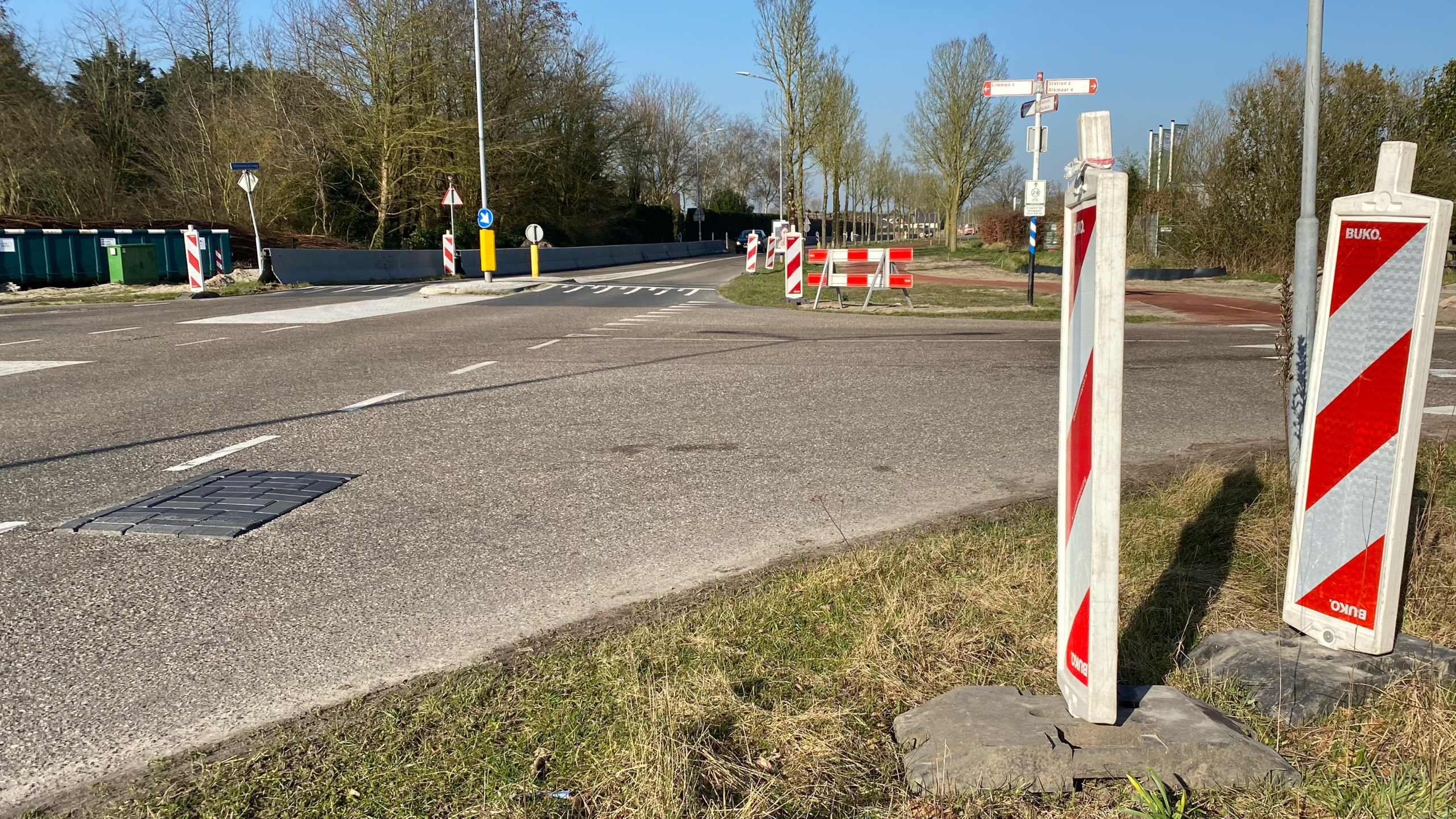 Straatwerkzaamheden met rood-witte afzetpalen en verkeersborden op een weg met bomen in de achtergrond.