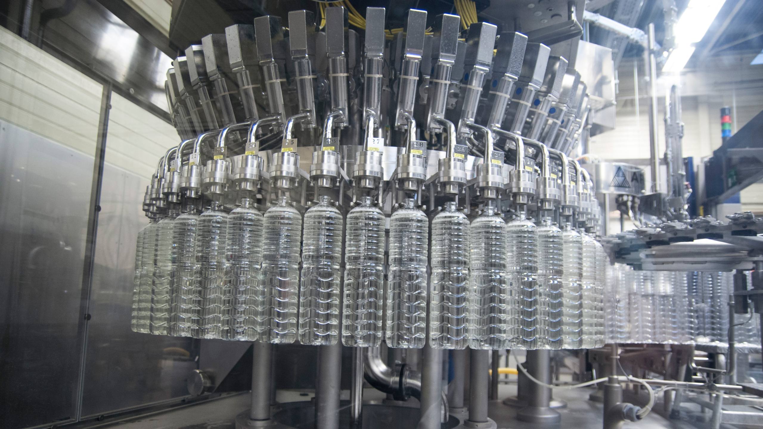 Rij met doorzichtige plastic flessen die door een industriële vulmachine worden gevuld in een fabriekshal.