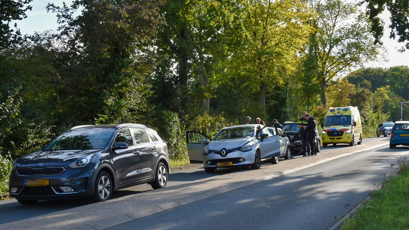 Auto-ongeluk op een weg met drie auto's betrokken, politieagenten en een ambulance aanwezig aan de kant van de weg om te assisteren.