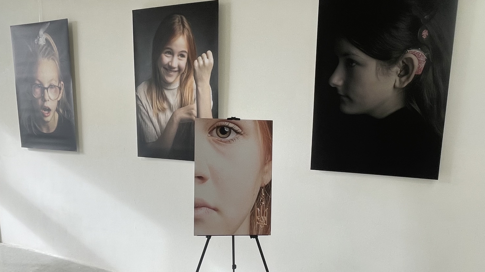 Tentoonstelling in een gang met meerdere portretten van kinderen aan de muur en een foto op een ezel erop gericht.