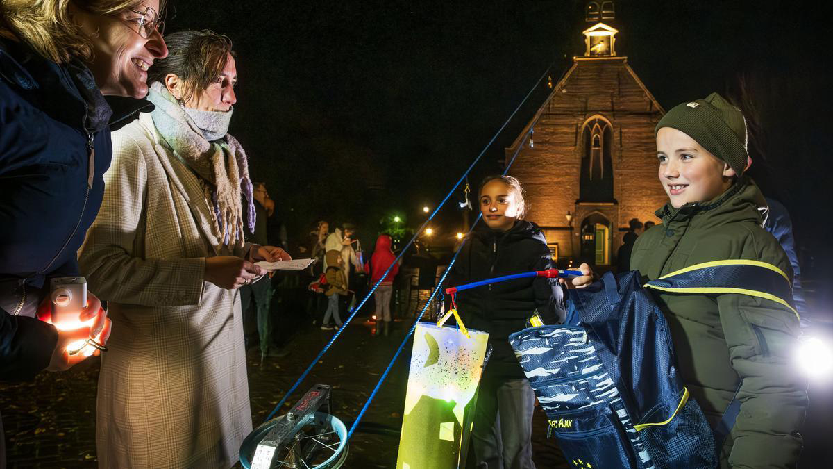 Kinderen en volwassenen dragen lampionnen tijdens een evenement in de avond bij een verlichte kerk.