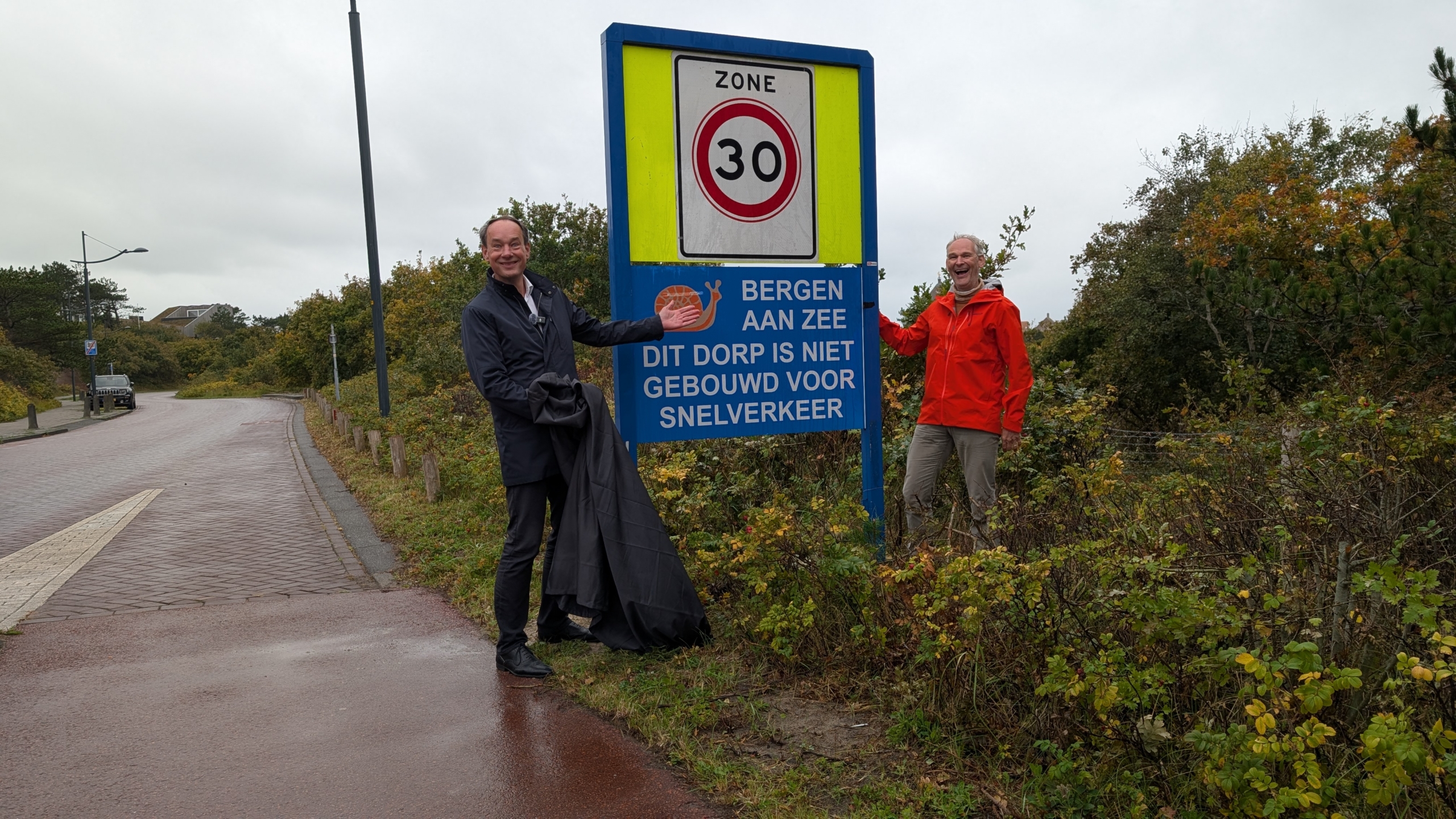 Twee mannen staan naast een bord dat de snelheid in Bergen aan Zee tot 30 km per uur beperkt, met de tekst "Dit dorp is niet gebouwd voor snelverkeer."