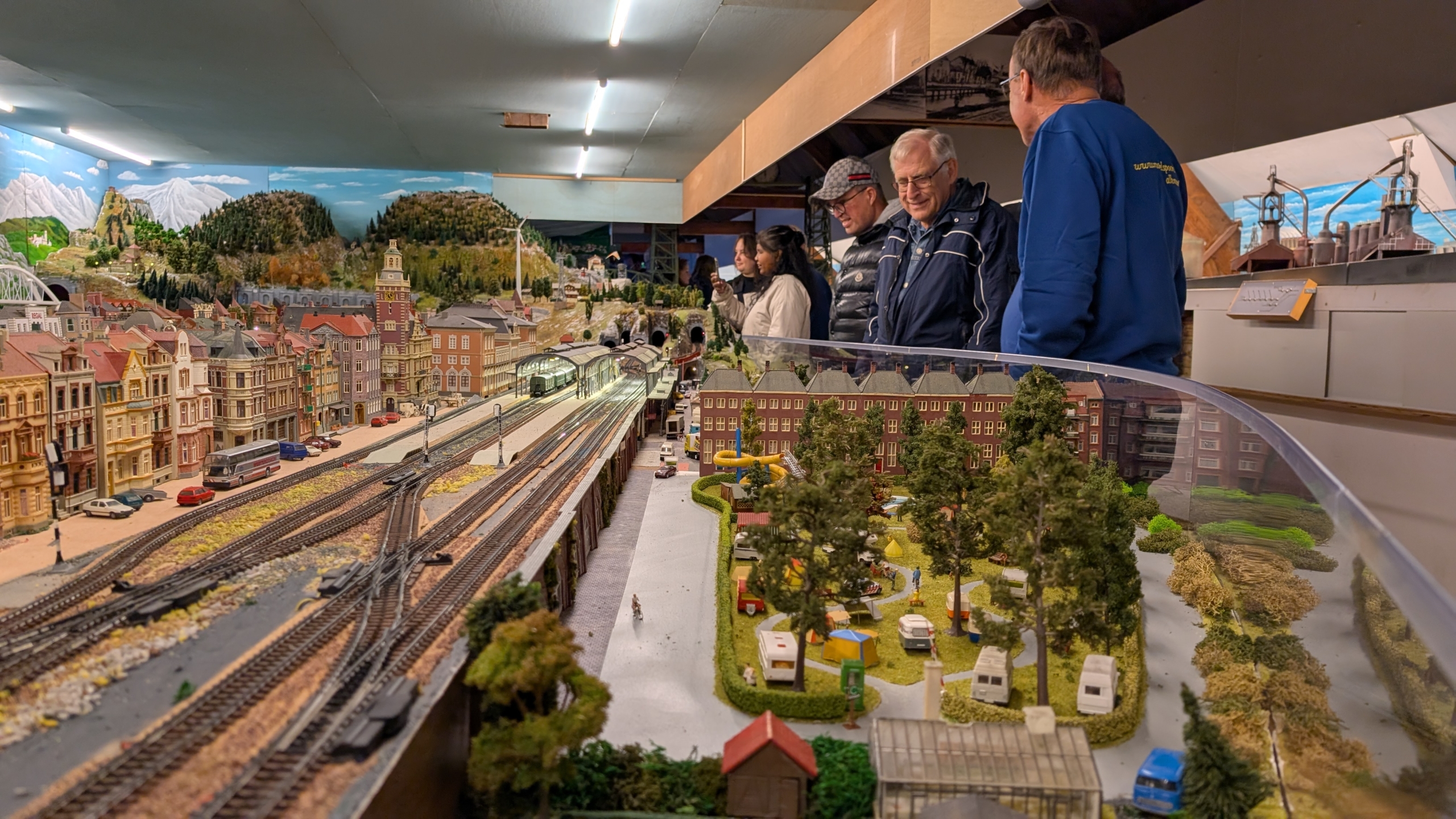 Mensen bekijken een gedetailleerde modeltreinbaan met spoorwegen, landschappen en miniatuurgebouwen.