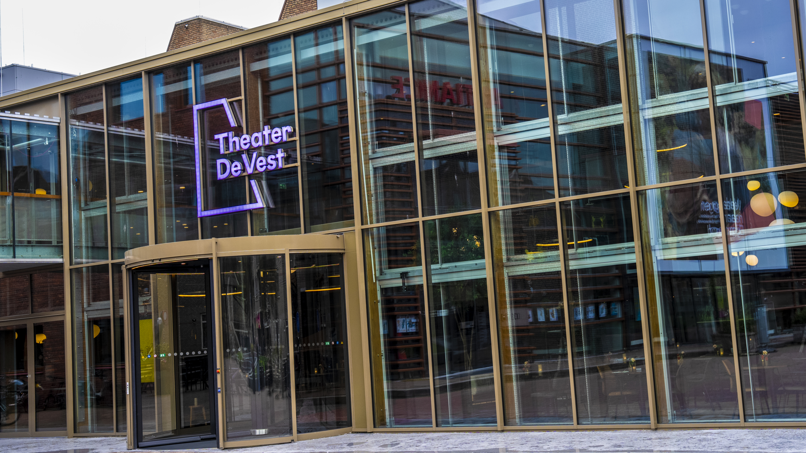 Gevel van Theater De Vest met glazen deuren en ramen, onder een bewolkte hemel.