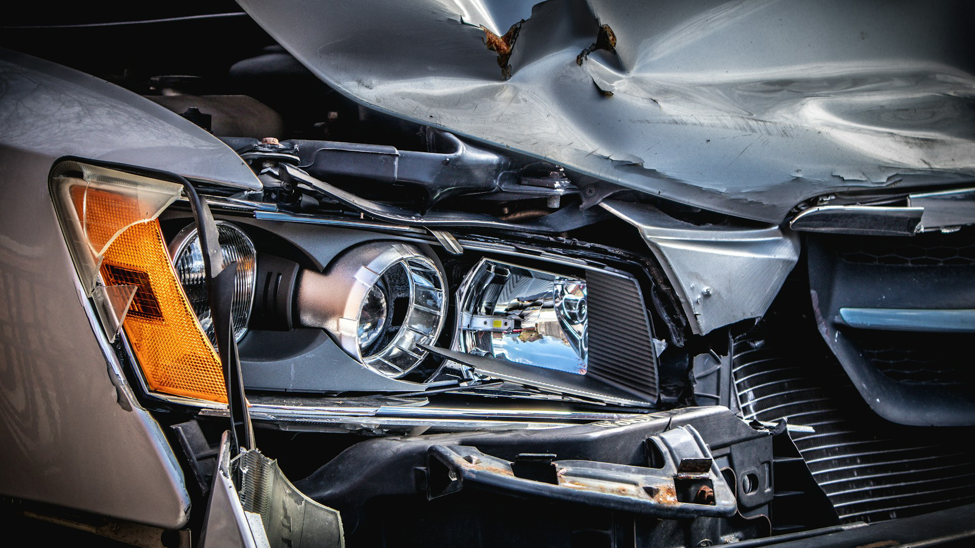 Een close-up van een beschadigde koplamp en gebogen carrosserie van een auto na een botsing.