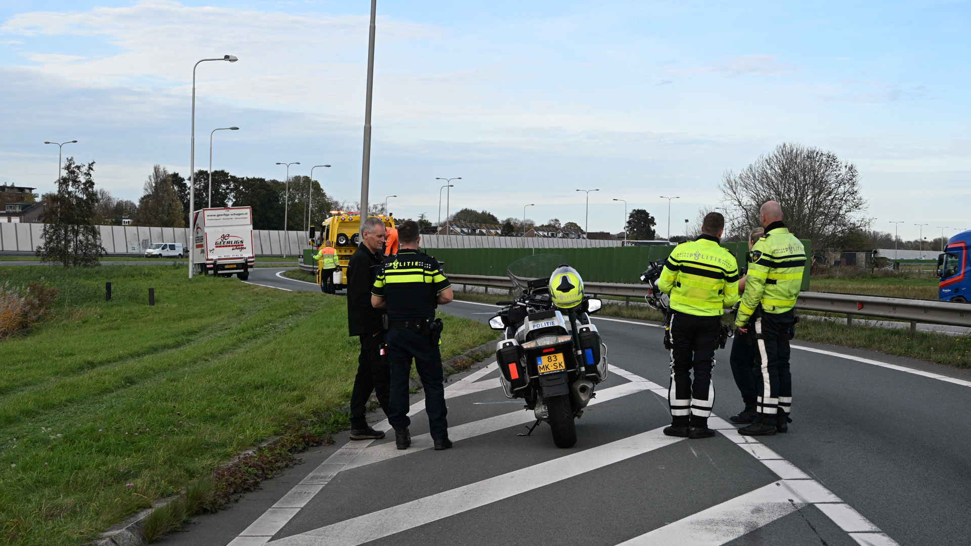 Politieagenten staan op een afrit bij een vrachtwagen die ingrijpen vereist, met een politiemotor op de voorgrond.